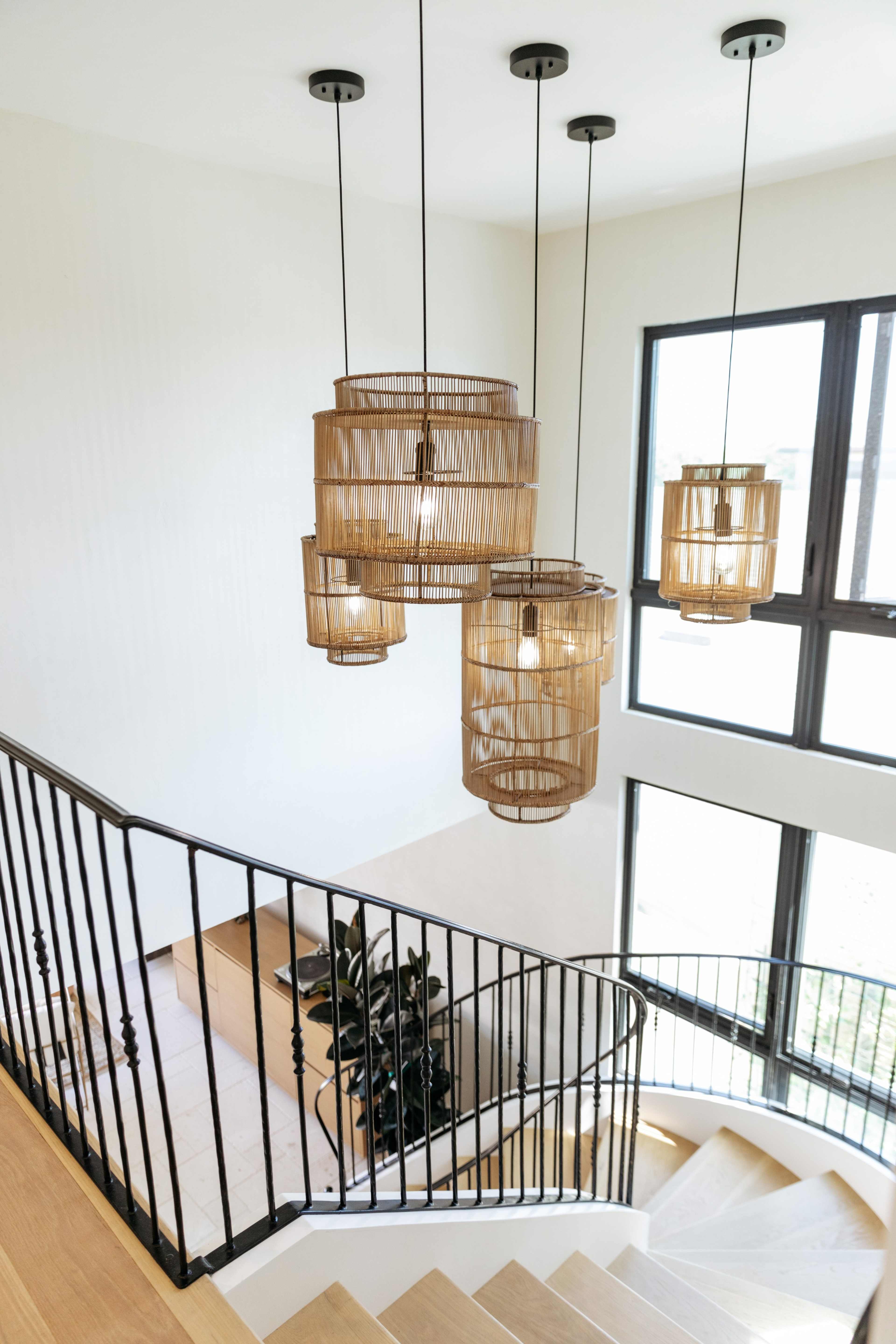 A staircase with wooden steps and four hanging rattan chandeliers, illuminated by natural light from large windows.