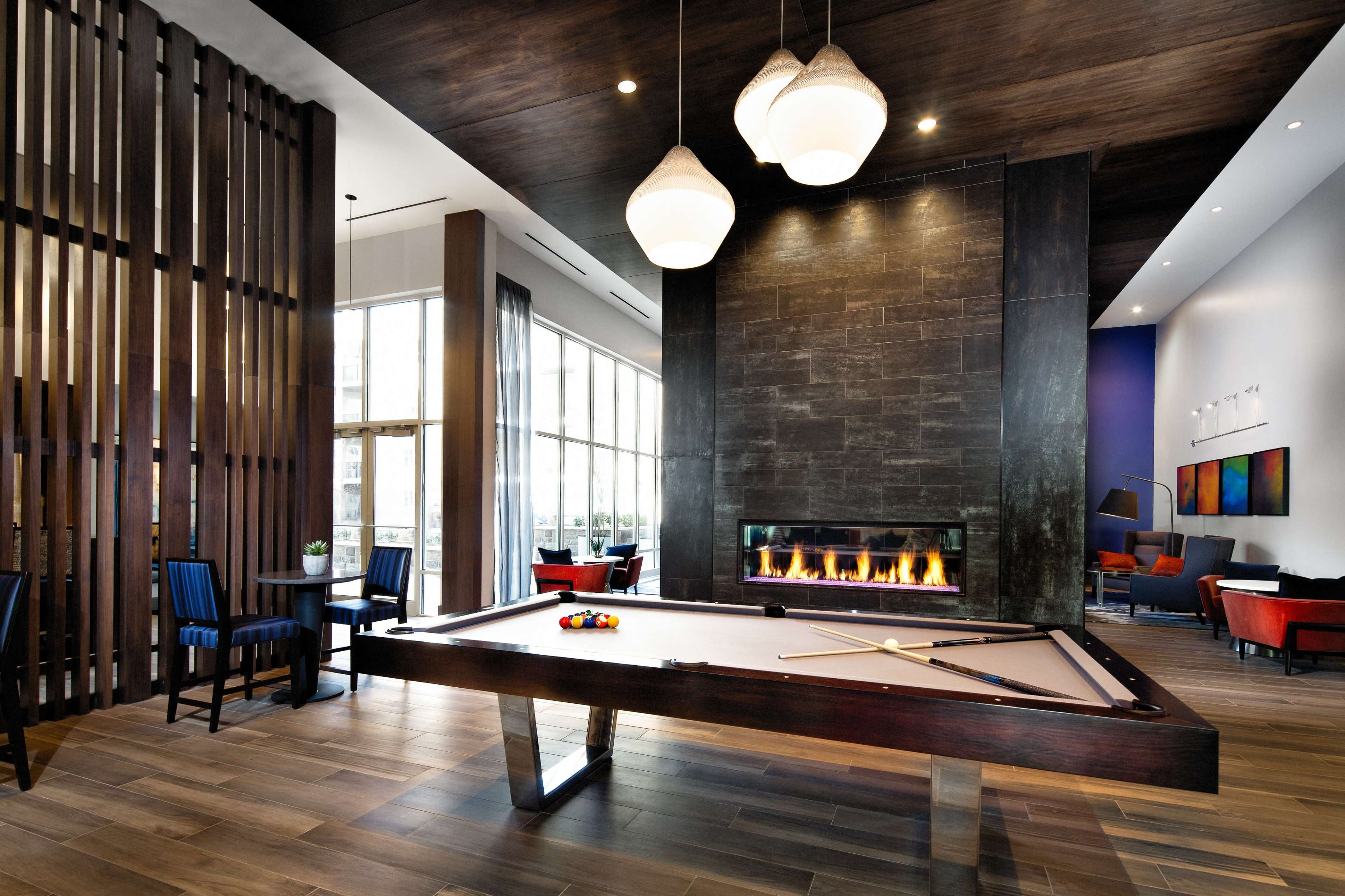 A modern lounge area featuring a pool table, a fireplace, and seating arrangements with large windows that allow natural light to filter in.