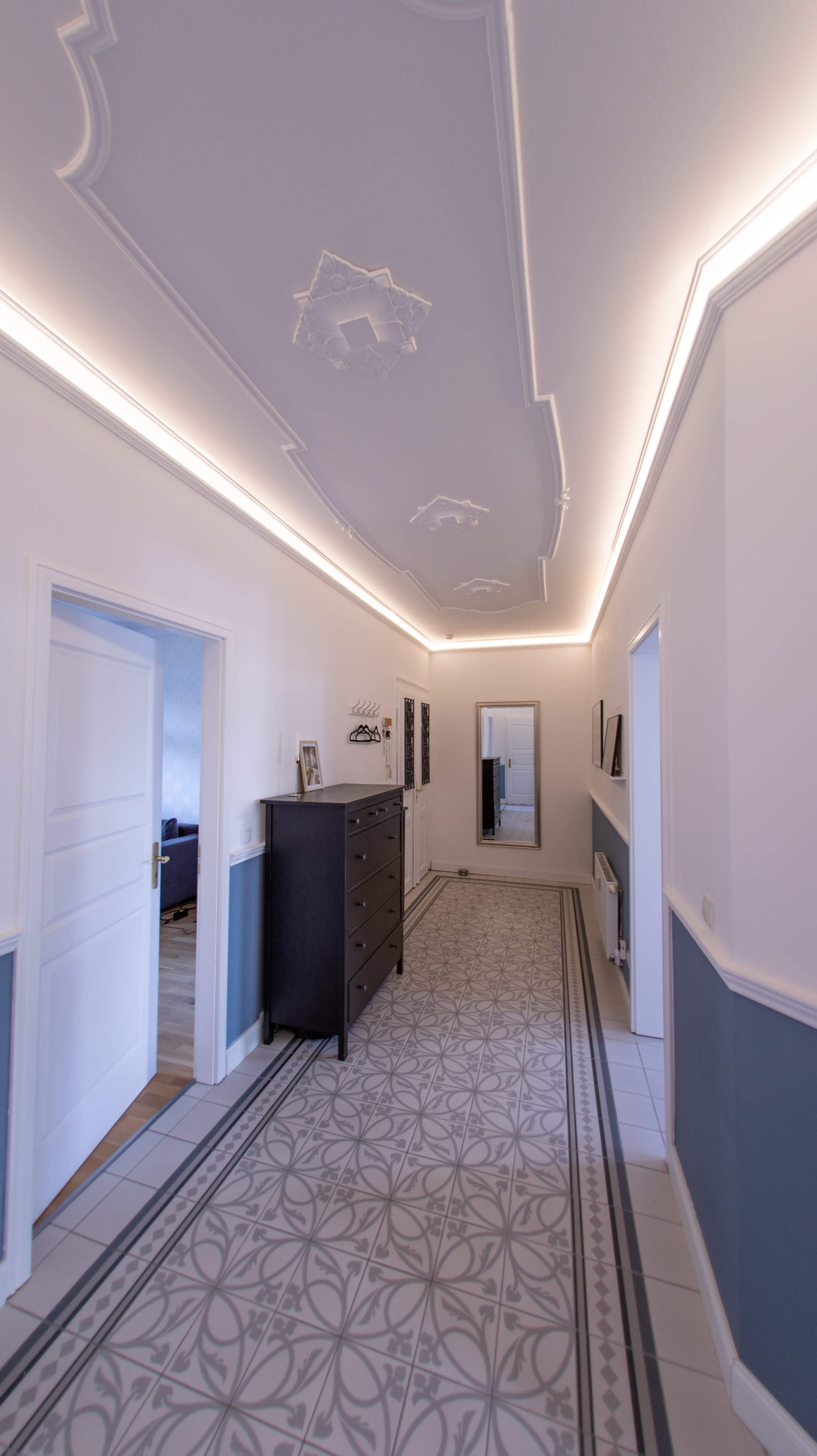 The image shows a well-lit hallway with decorative ceiling moldings and a tiled floor featuring a geometric pattern.