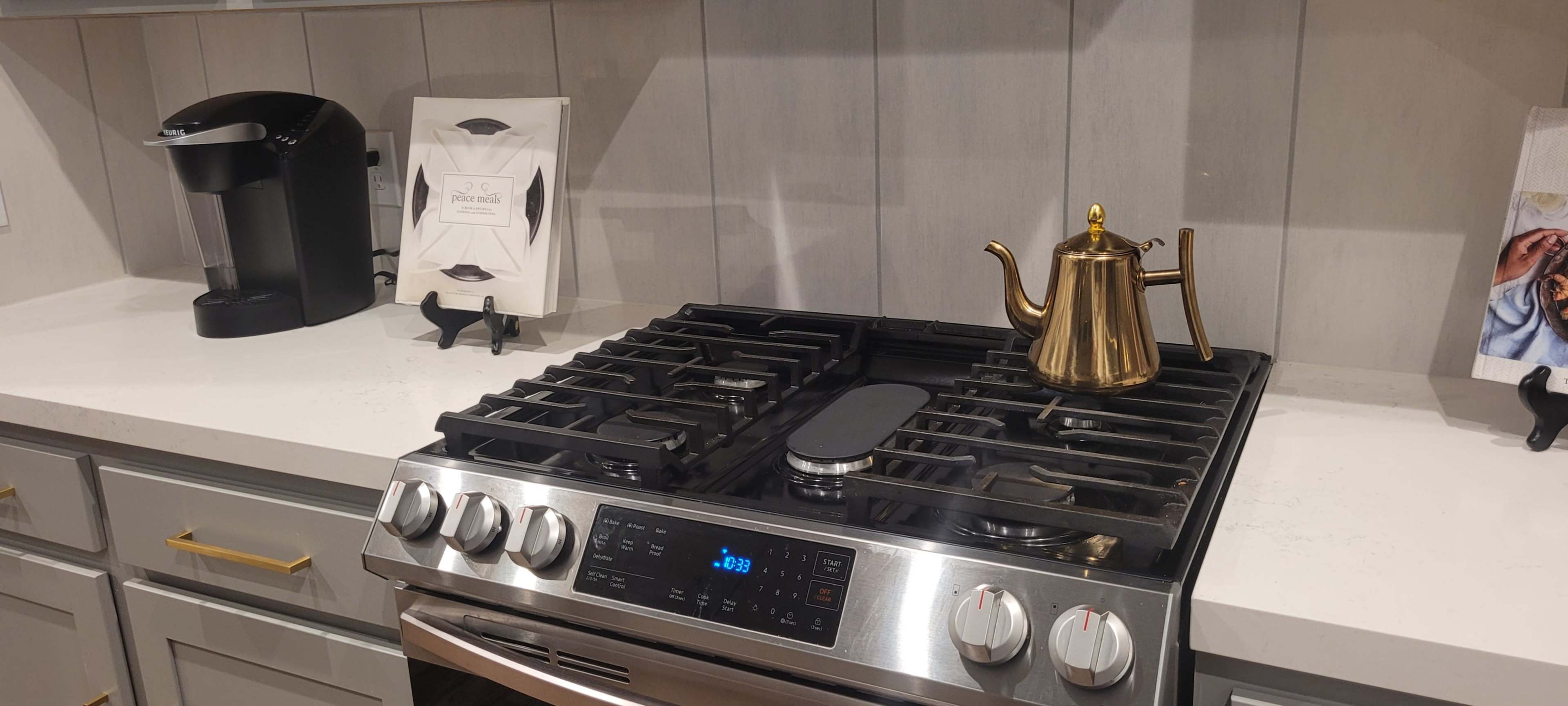 A modern kitchen stove with a shiny golden kettle on it, alongside a coffee maker and a decorative frame on the counter.