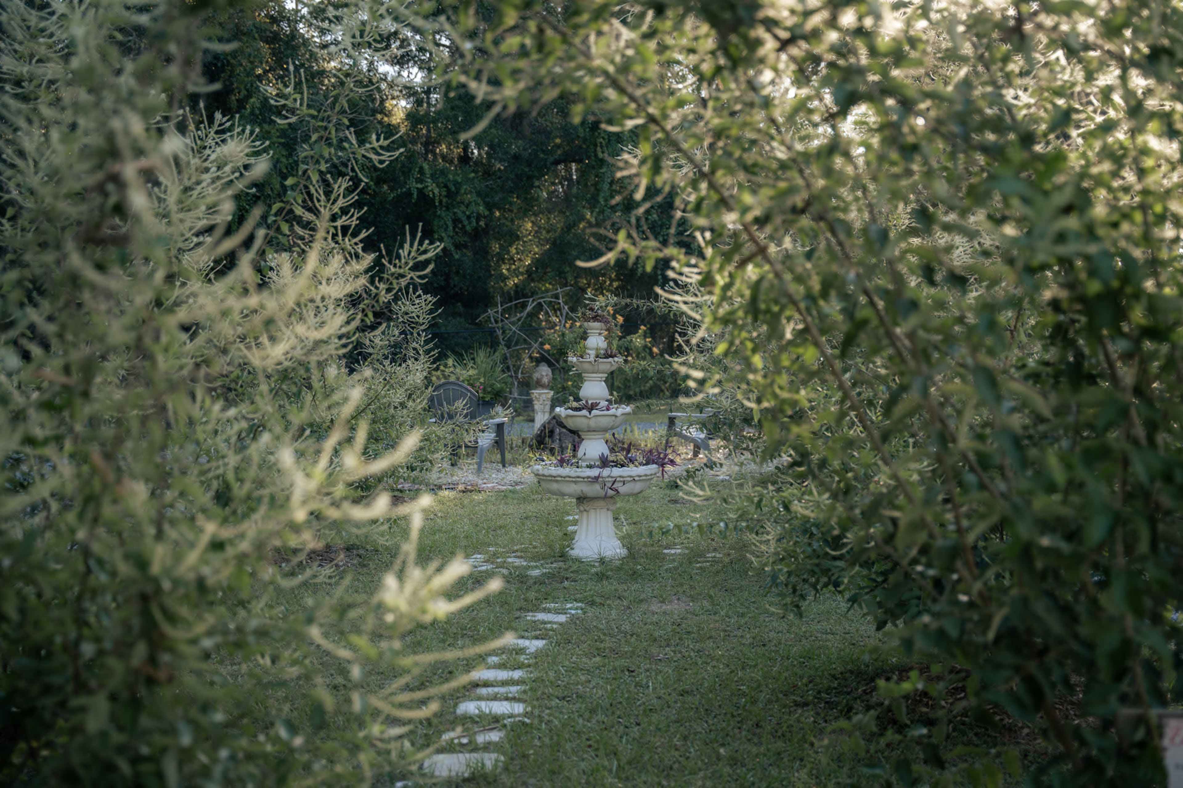 A stone fountain is surrounded by greenery and a pathway in a tranquil garden setting.