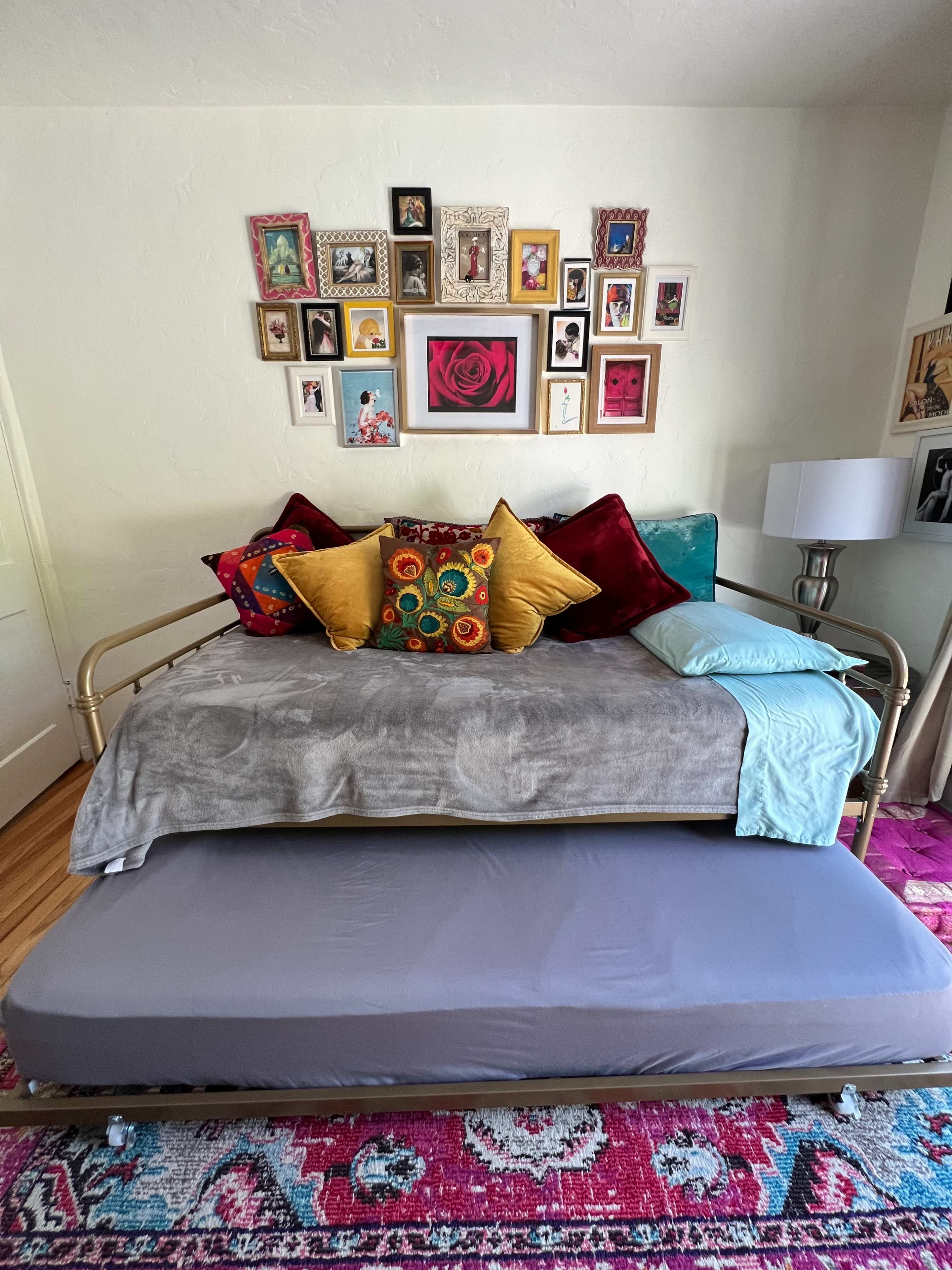 A daybed adorned with decorative pillows is positioned against a wall featuring a gallery of framed photos and artwork.