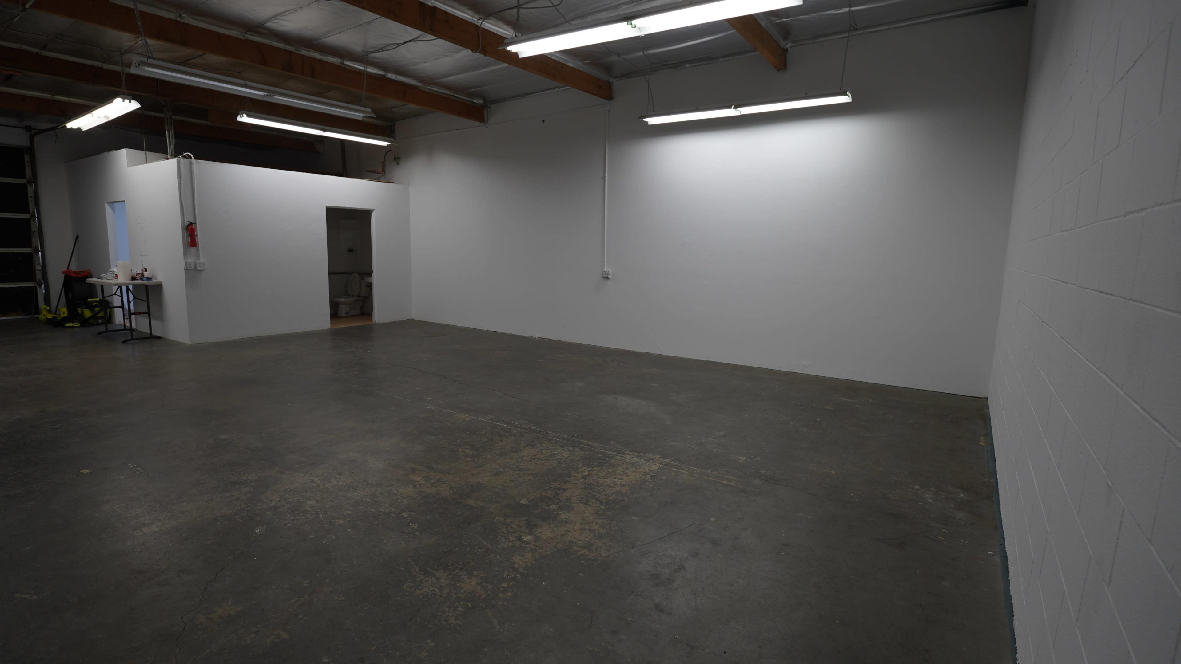 The image shows an empty industrial space with a concrete floor, white walls, and a small doorway leading to another room.