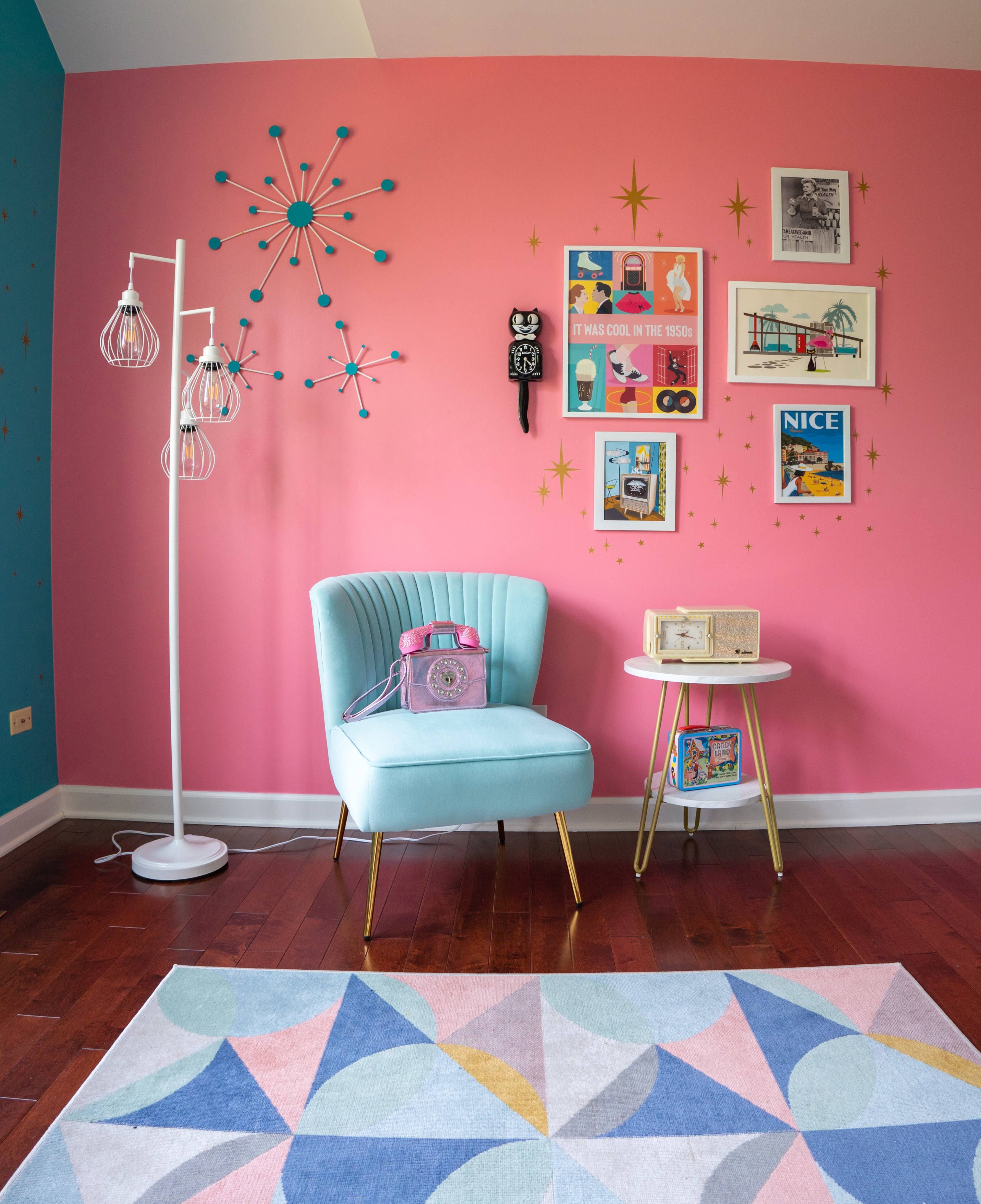 A colorful room featuring a light blue armchair, a small side table, retro decor on the walls, and a starburst wall clock.