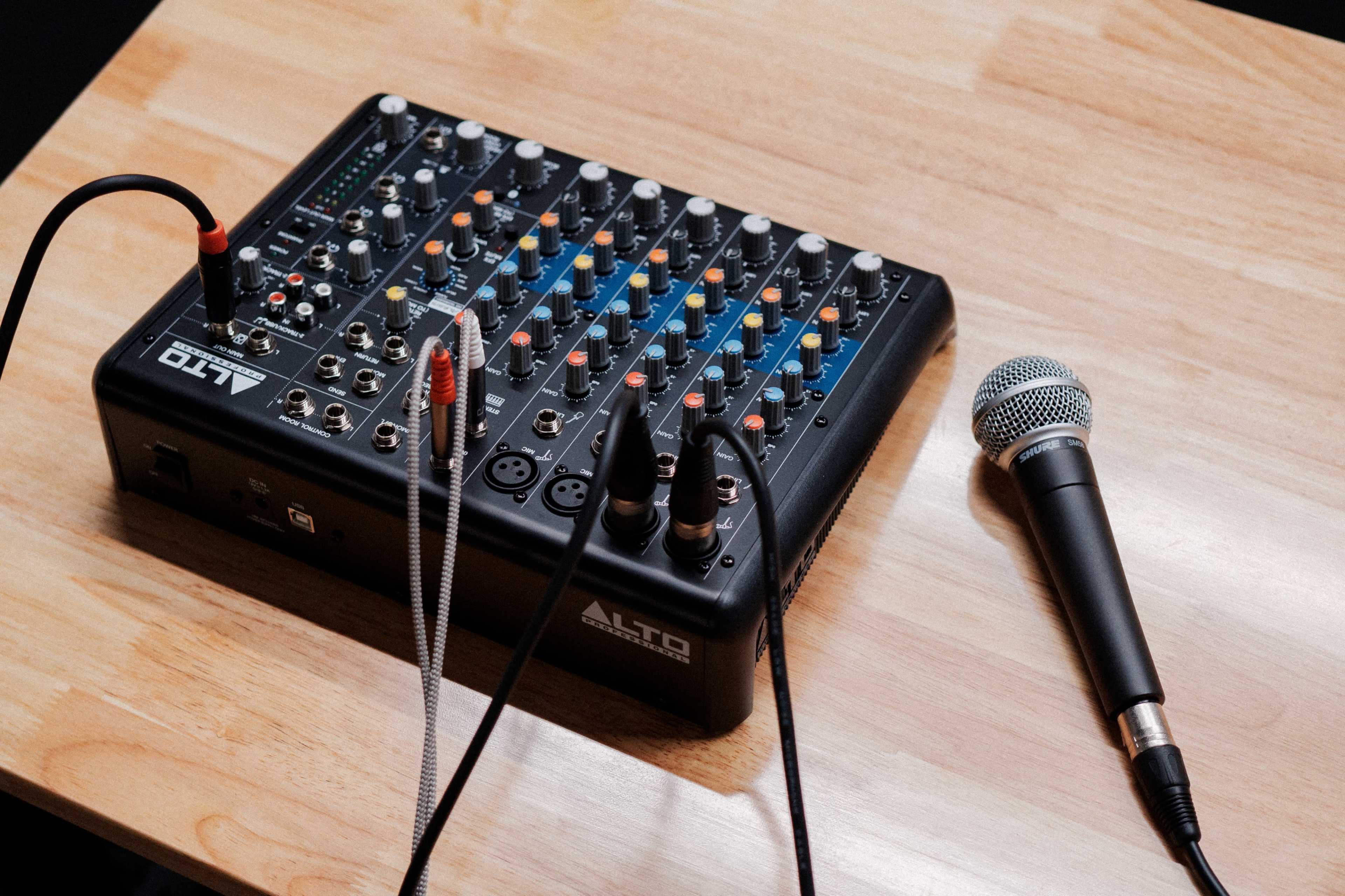 A black audio mixer sits on a wooden table next to a microphone.