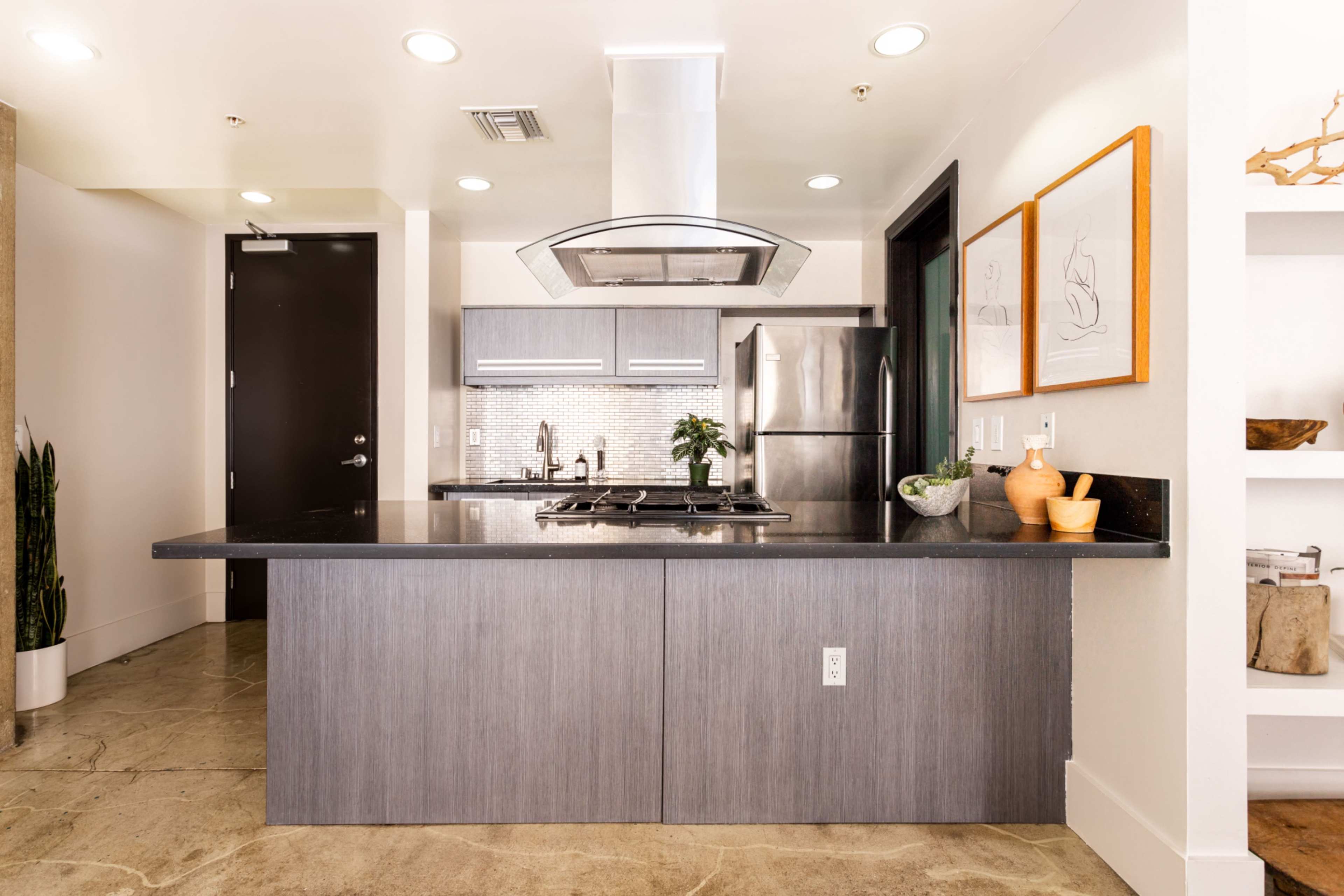 A modern kitchen features a central island with a stovetop, stainless steel appliances, and minimalist cabinetry.