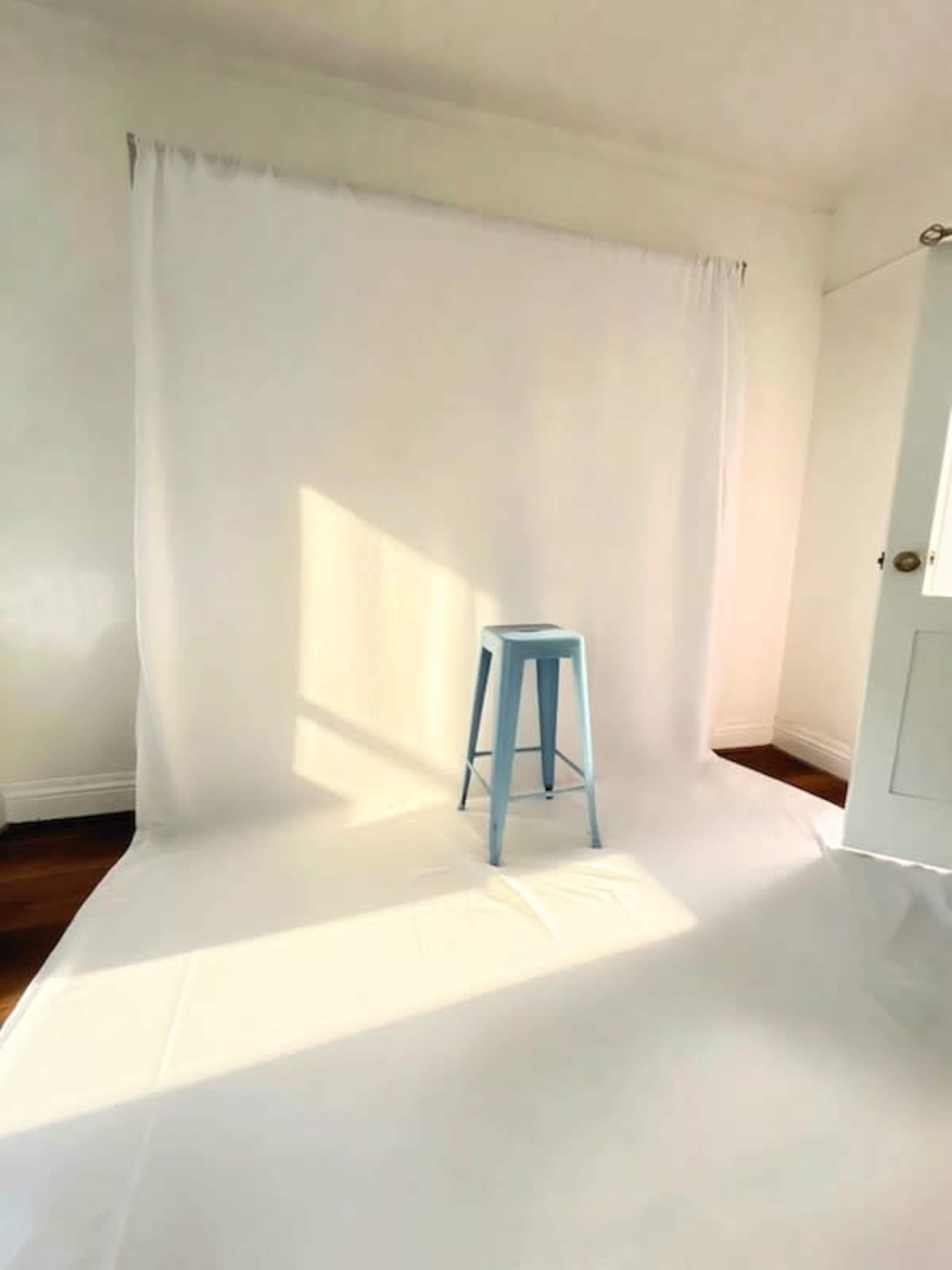 A blue stool is positioned on a white backdrop in a well-lit room.