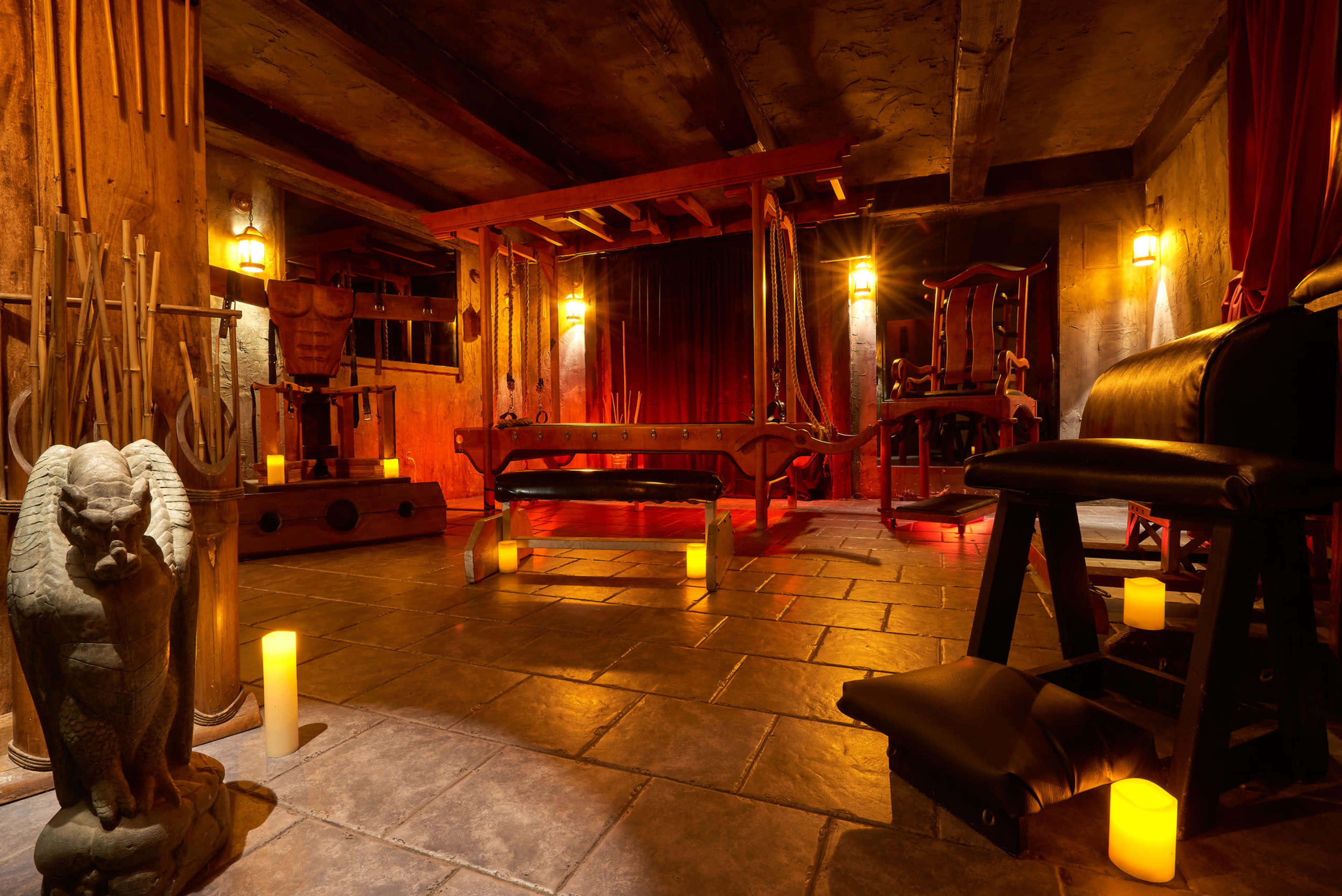 The image depicts a dimly lit room featuring wooden apparatus and stone flooring, illuminated by candles arranged around the space.