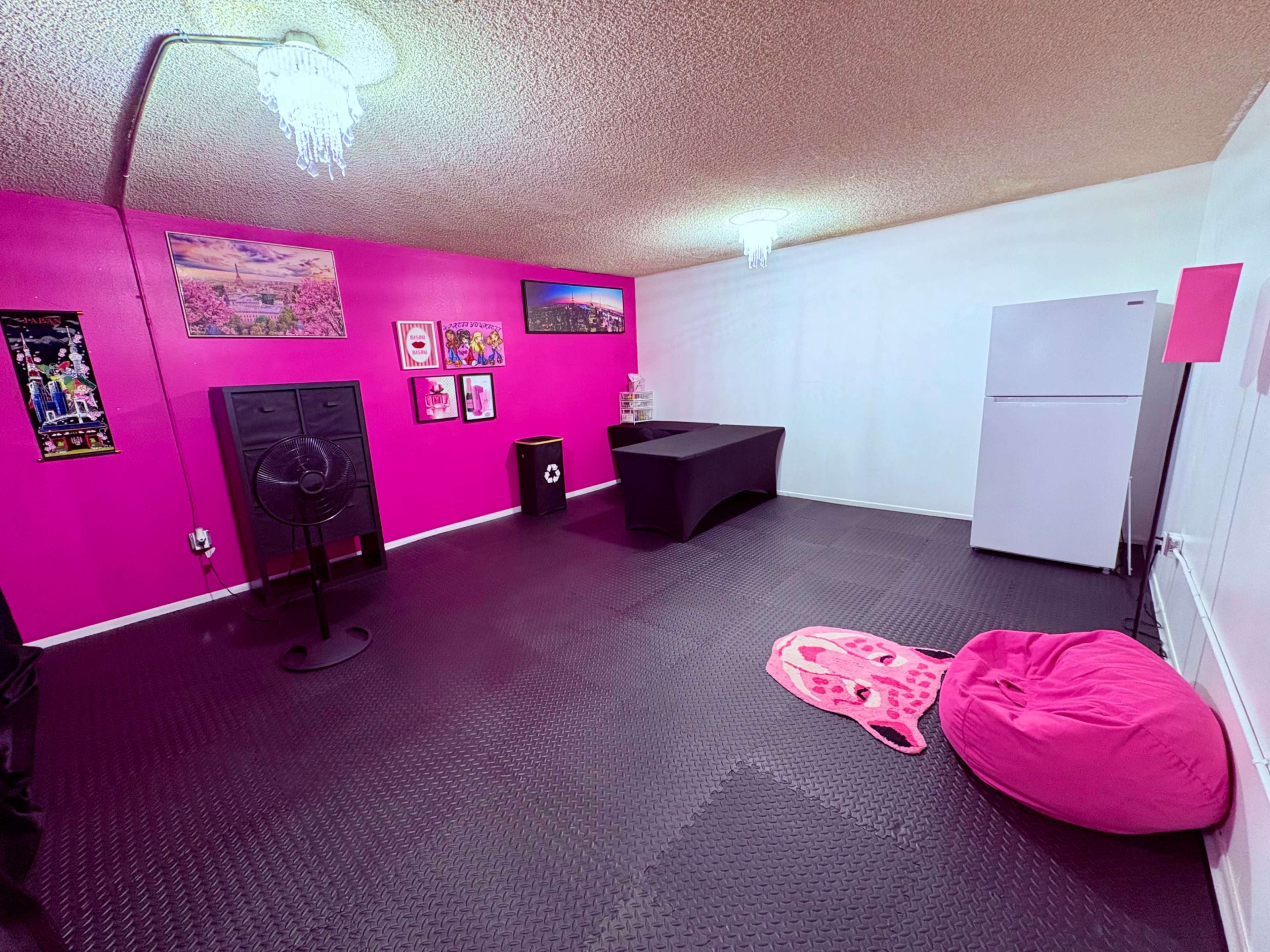 The image shows a room with pink walls, black rubber flooring, a table, a refrigerator, and a pink bean bag chair.