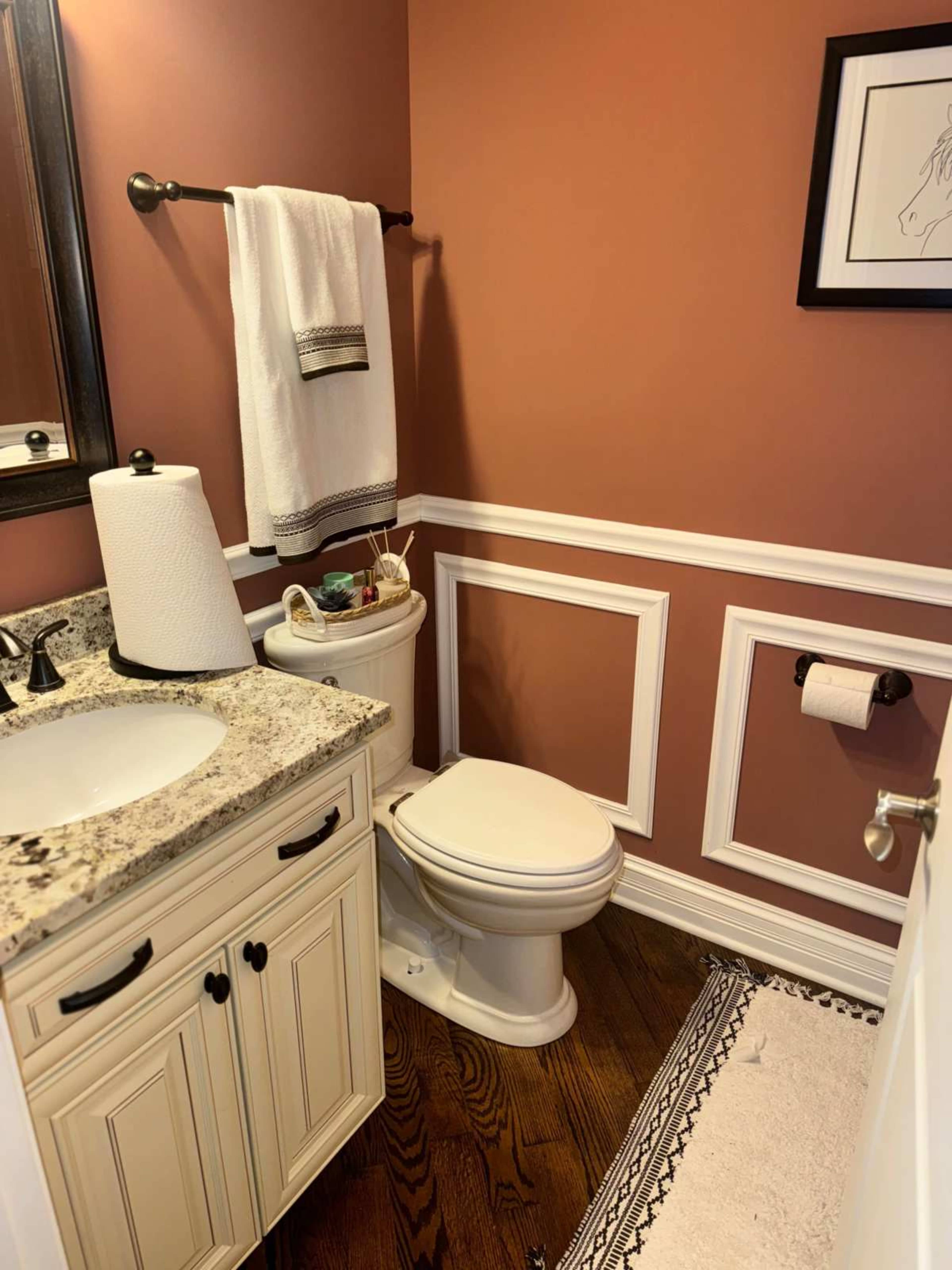 A small bathroom featuring a toilet, sink with a granite countertop, and decorative wall paneling in a warm color scheme.