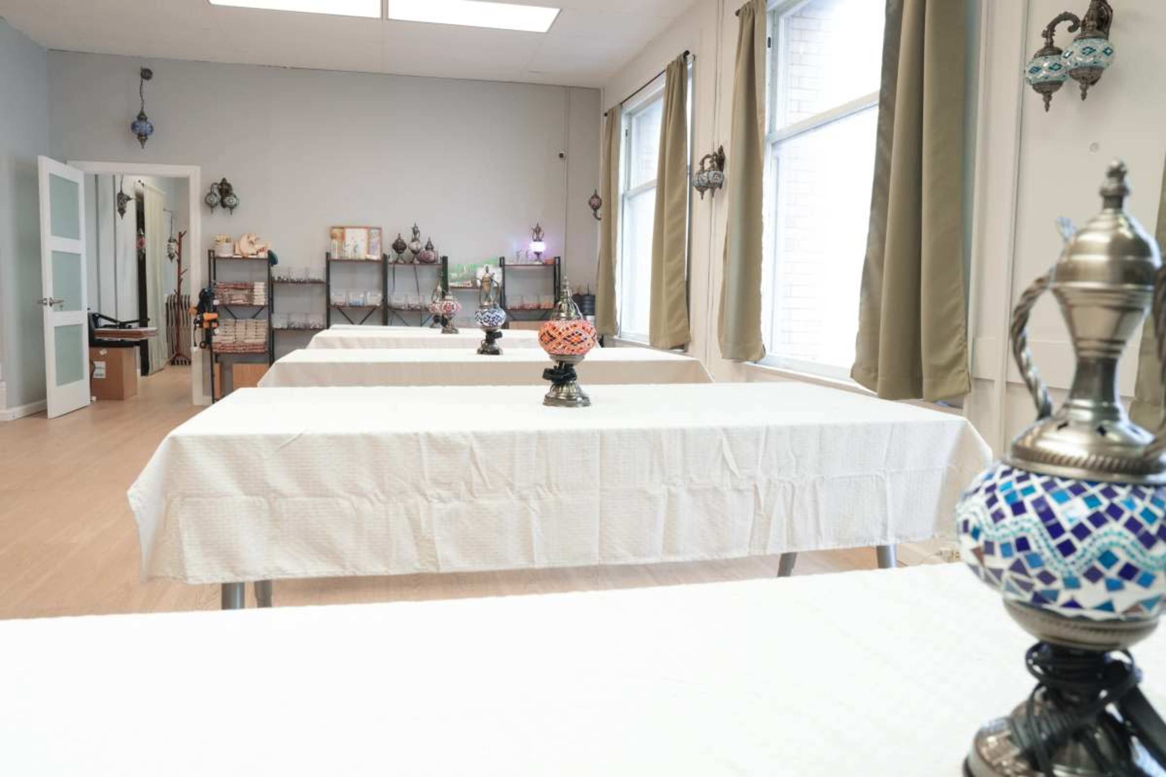 The image shows a spacious room with several tables covered in white tablecloths and decorative lamps placed in the center of each table.