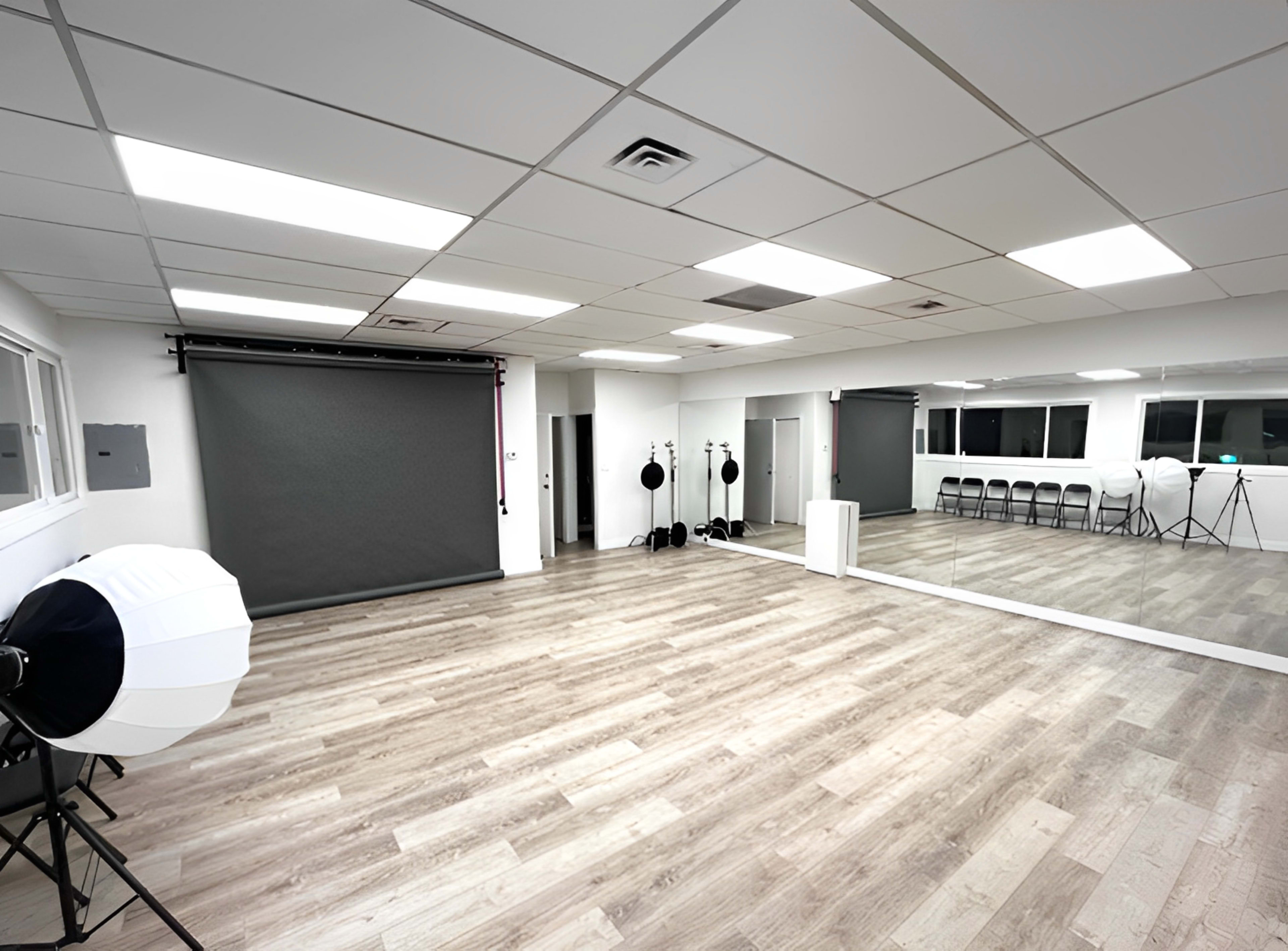 A spacious, well-lit studio with a black backdrop, mirrors, and photography equipment arranged neatly.