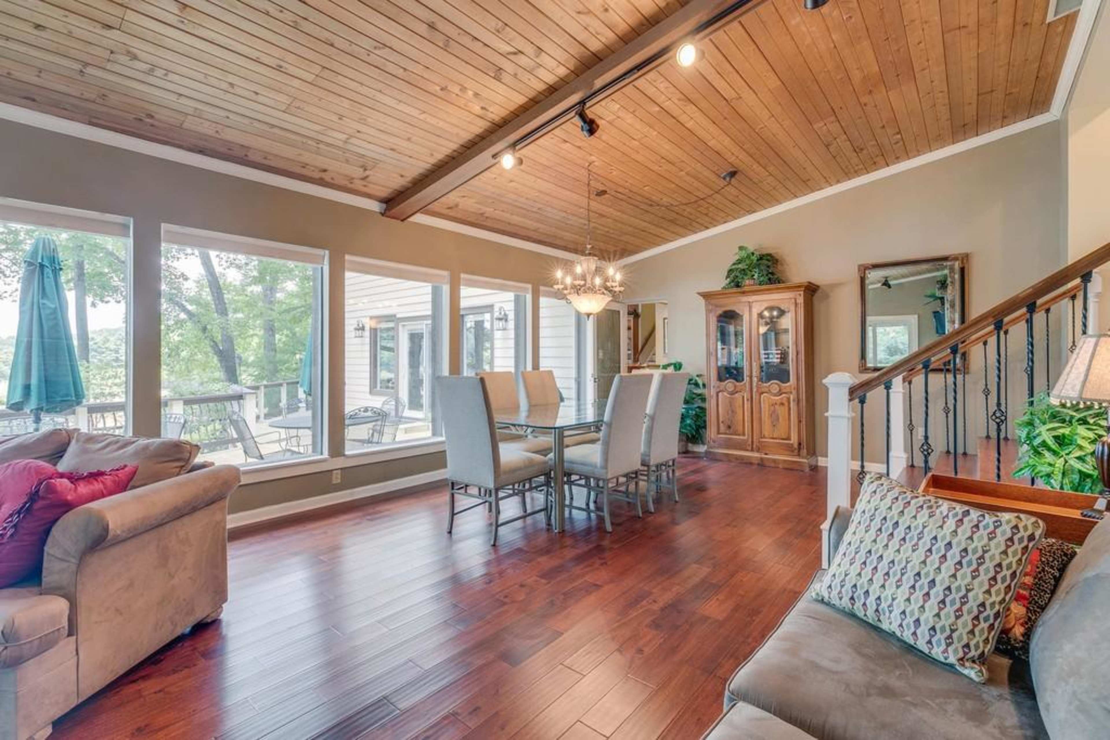 A spacious living and dining area with wooden flooring, a wooden ceiling, and large windows that provide a view of the outdoors.