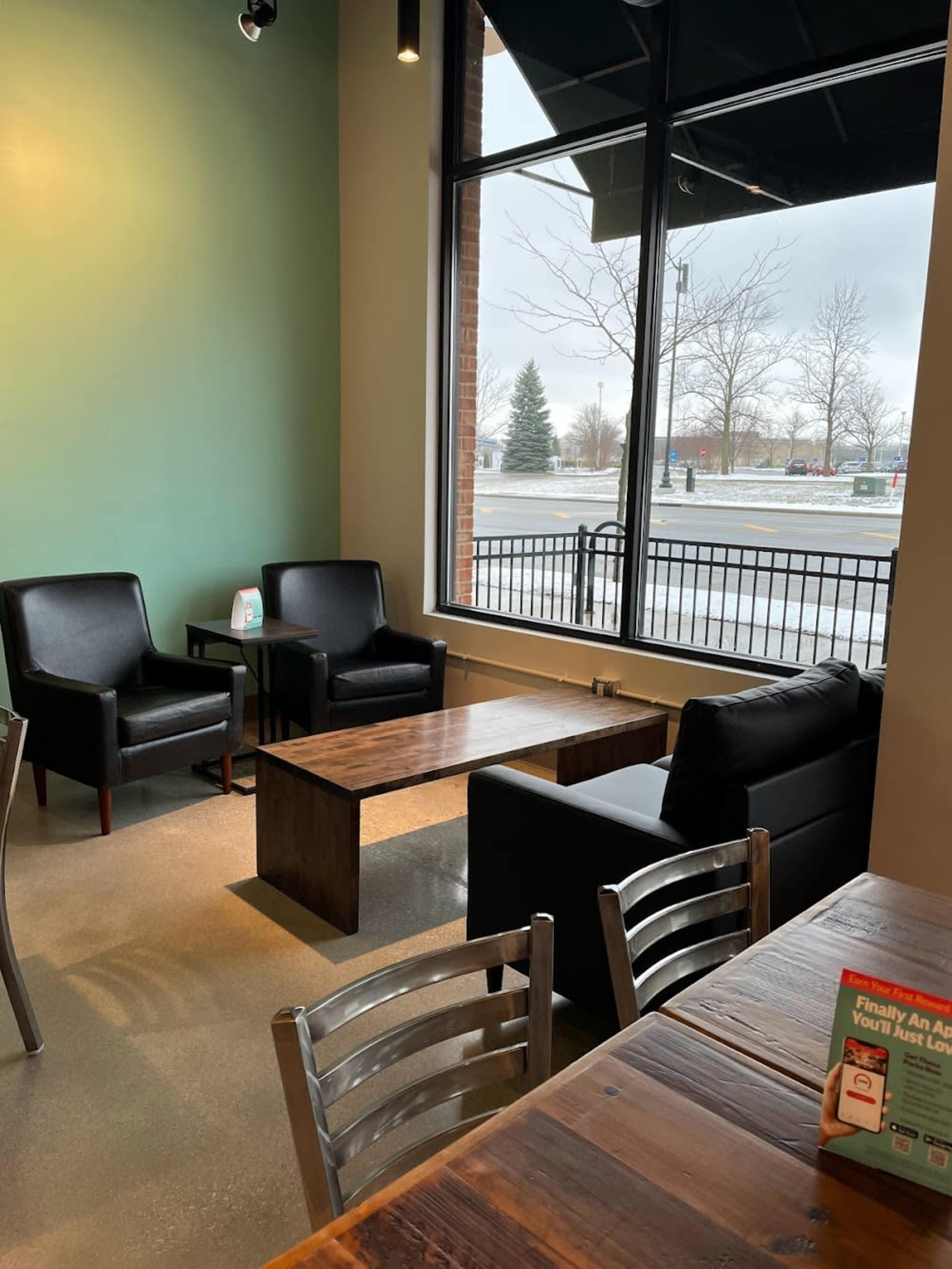 A cozy seating area in a cafe, featuring two black armchairs and a wooden coffee table under a large window.