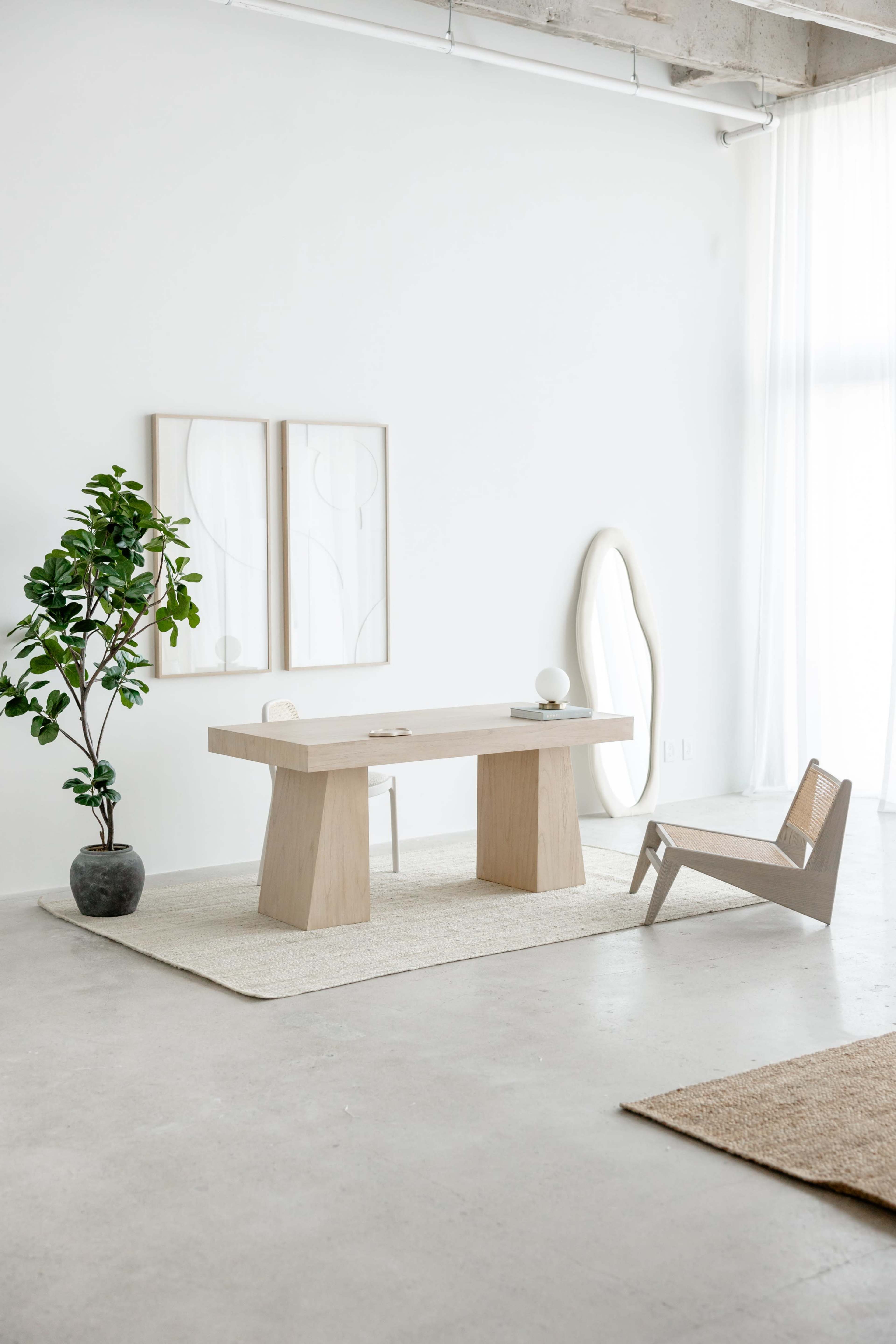 The image depicts a minimalist interior design featuring a light wooden table, a single modern chair, potted plant, and abstract art on the walls.