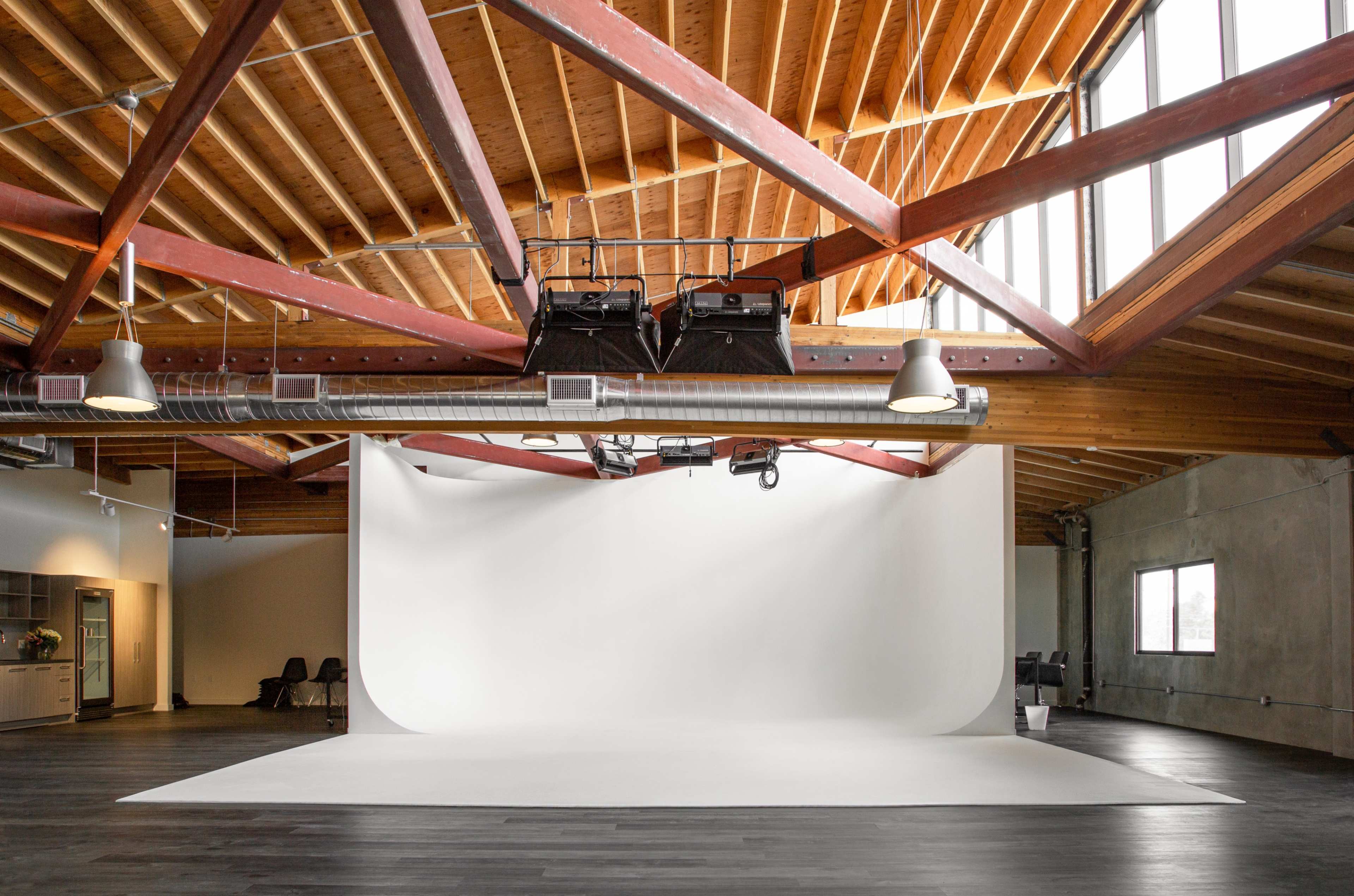 A spacious photography studio with a large white backdrop, wooden beams, and ample natural light from the windows.