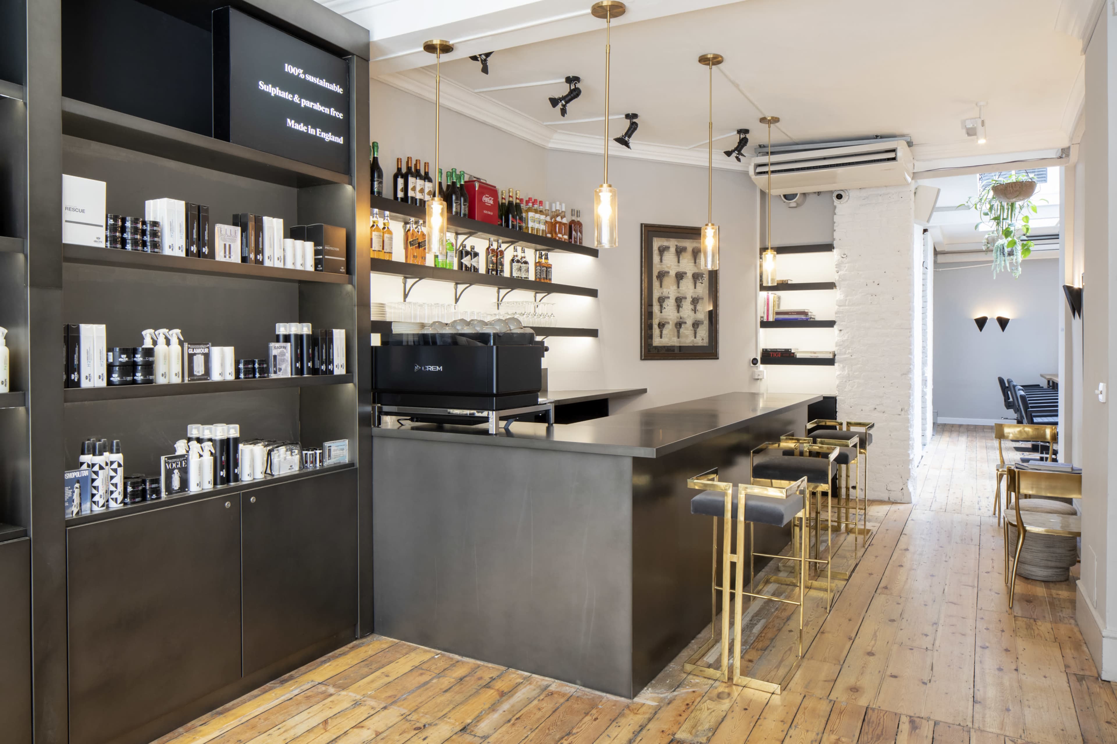 The image shows a modern cafe interior with a sleek bar, shelves displaying products, and wooden flooring.