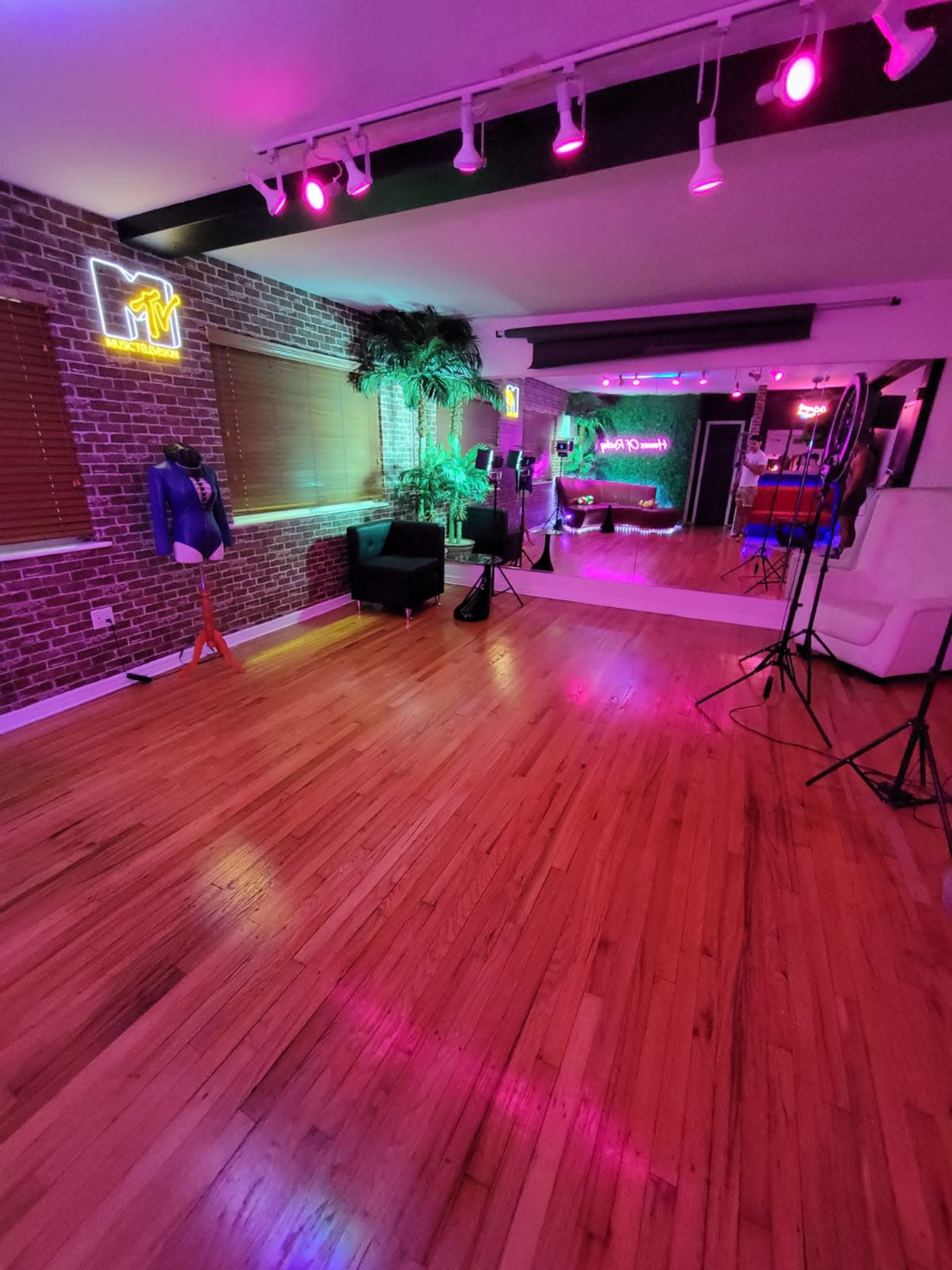 A vibrant studio space with wooden flooring, neon lights, and various decorative elements, including a couch and a backdrop for photography.