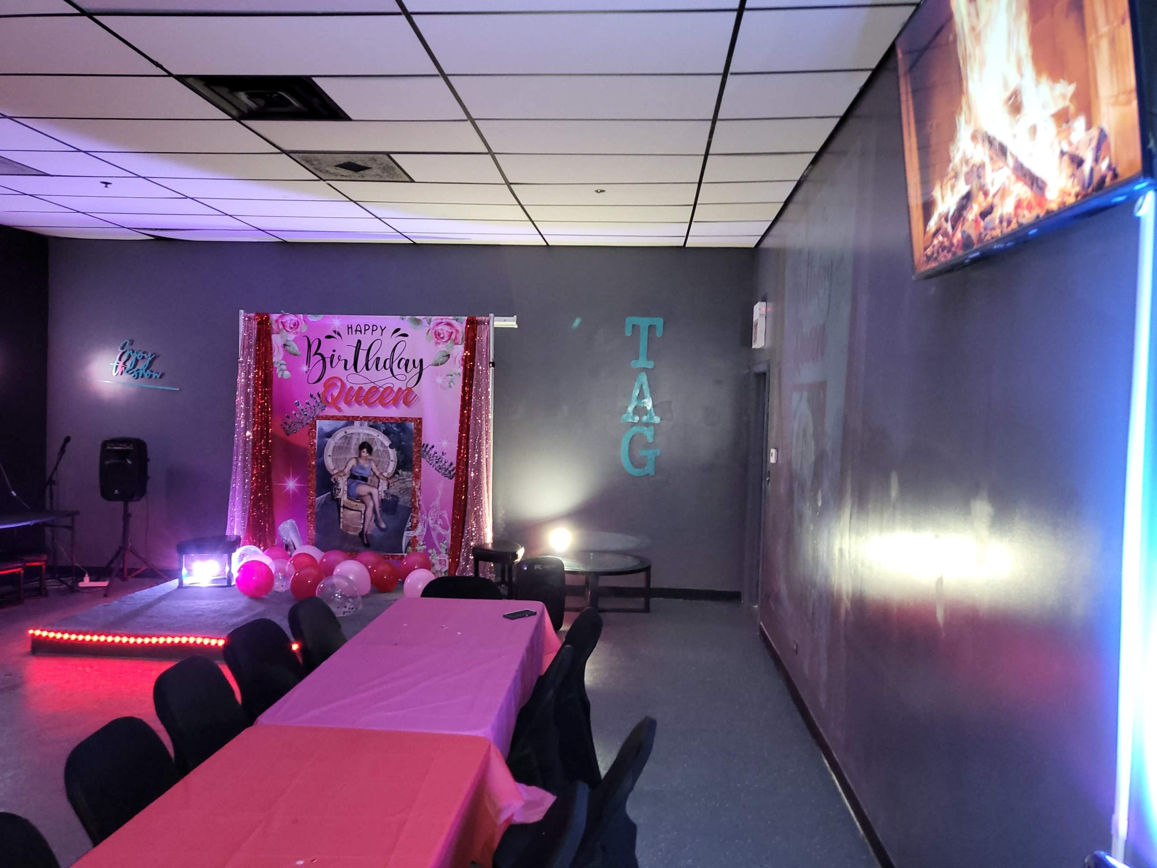 A decorated room for a birthday celebration, featuring a pink backdrop with "Happy Birthday Queen," a table with a pink tablecloth, and various balloons.