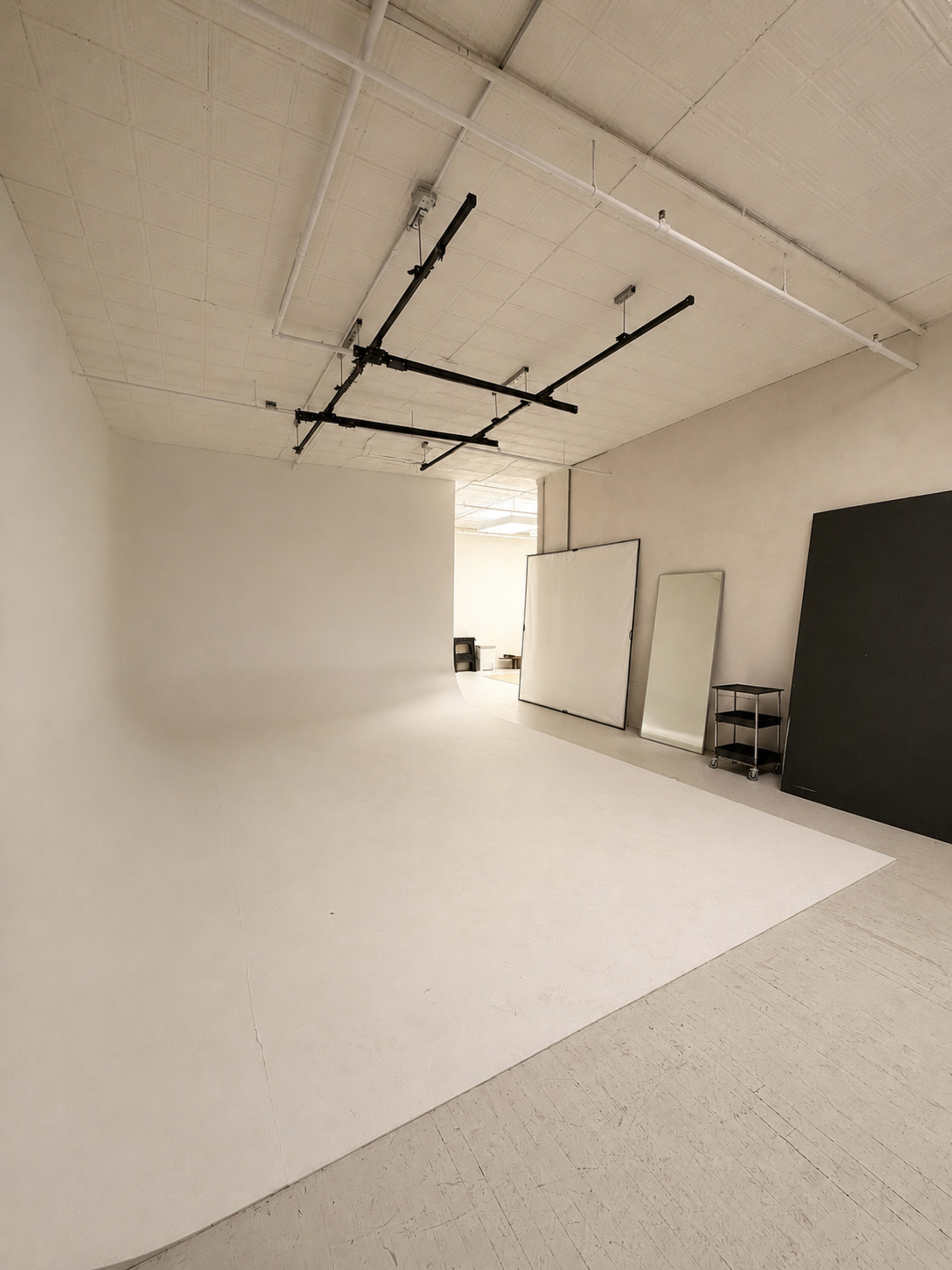 The image shows a spacious, minimalist photography studio featuring a large seamless backdrop, mirrors, and a small table in the corner.
