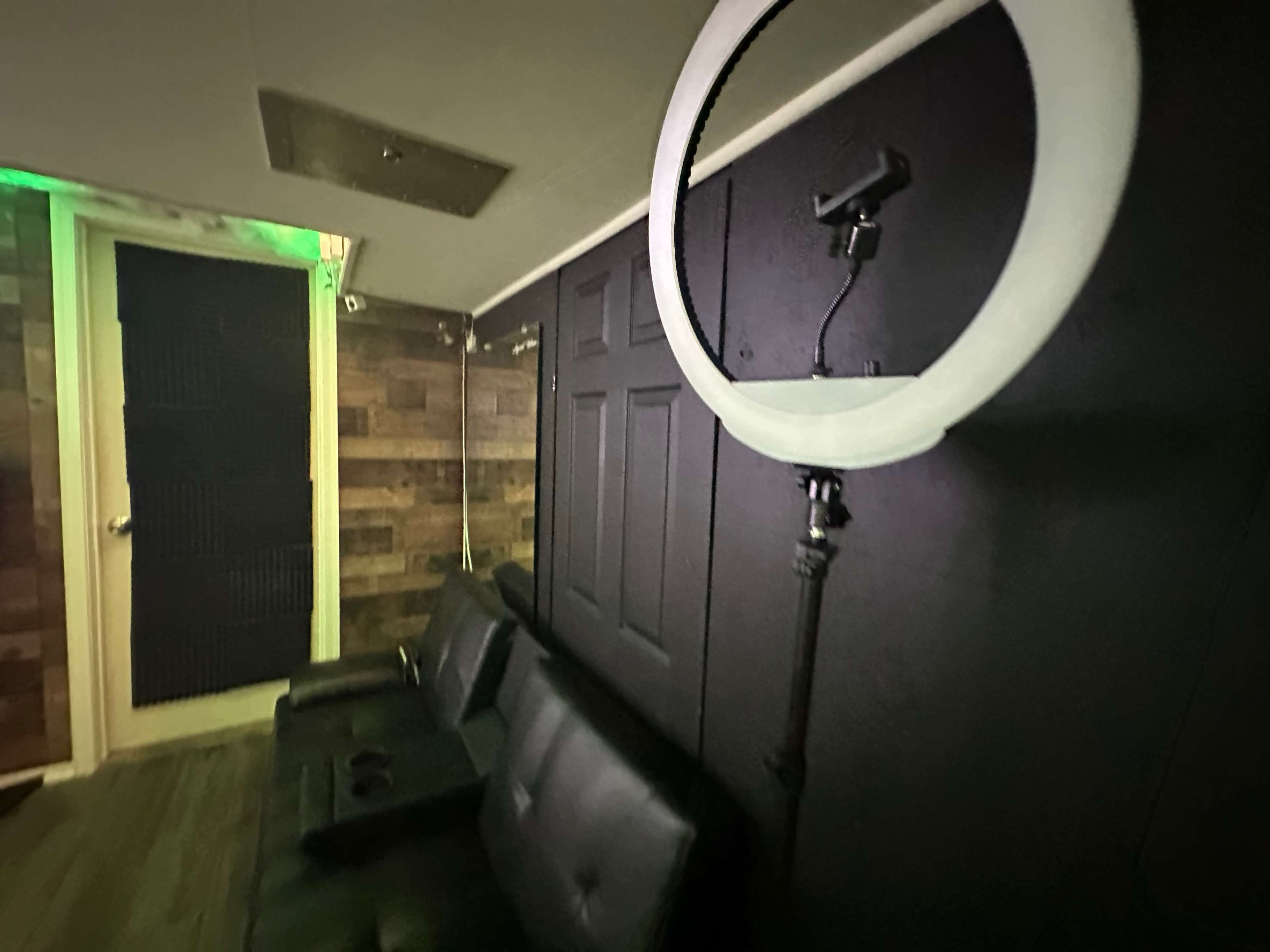 A small room with dark walls, a round ring light on a stand, and a black couch with armrests.