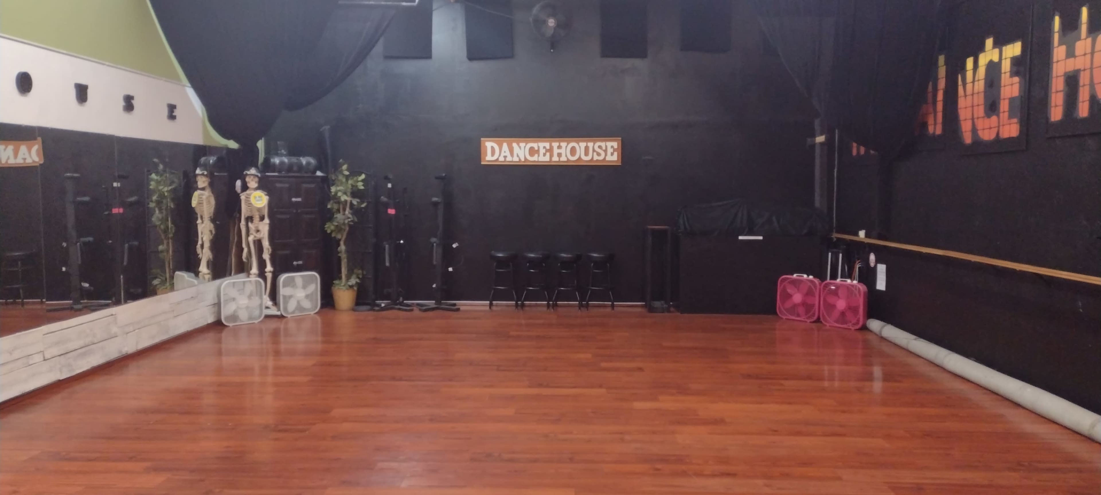 A dance studio with a polished wooden floor, black walls, a sign that reads "DANCE HOUSE," and various dance equipment arranged in the corner.
