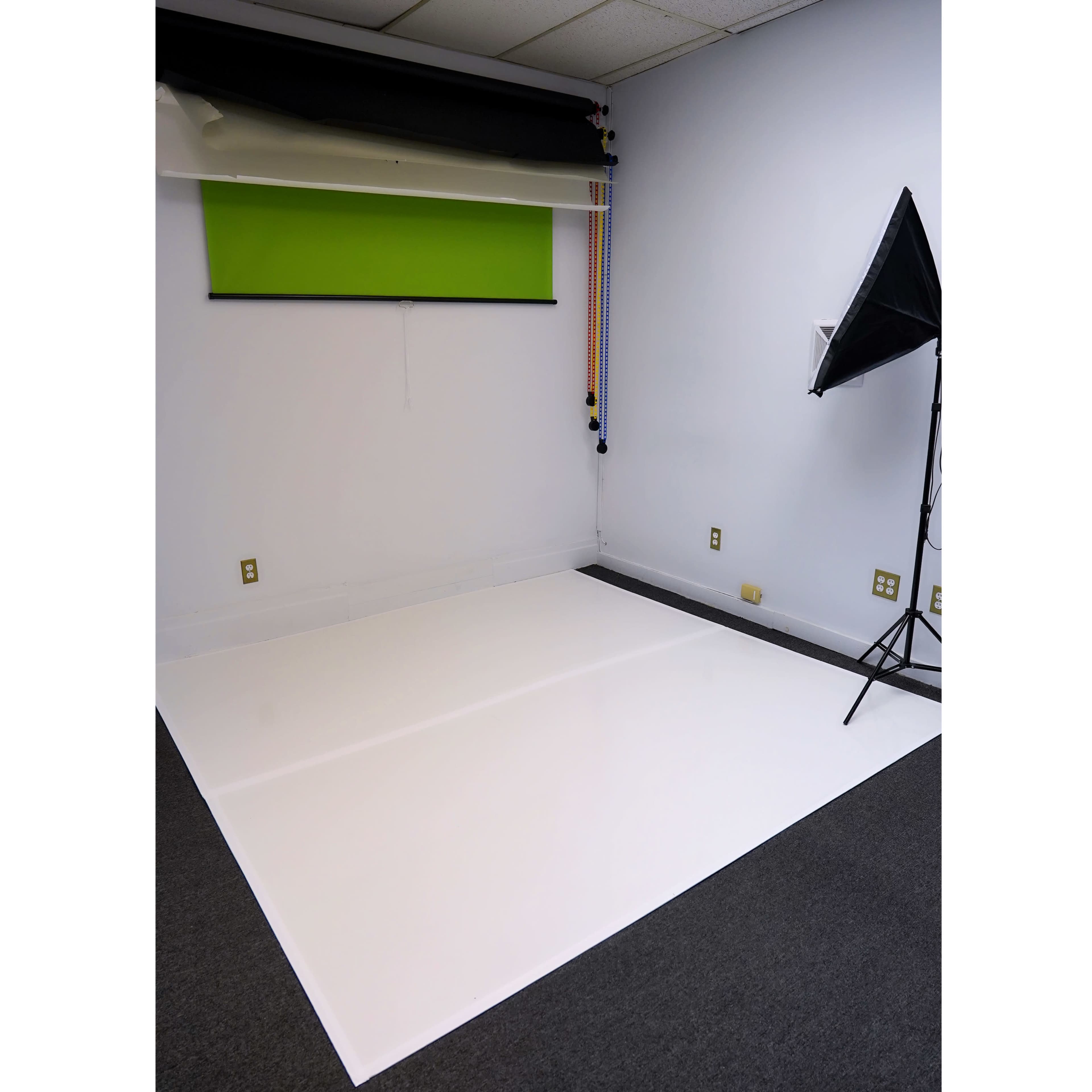 The image shows a photography studio with a white floor, a green backdrop, and a lighting setup in the corner.
