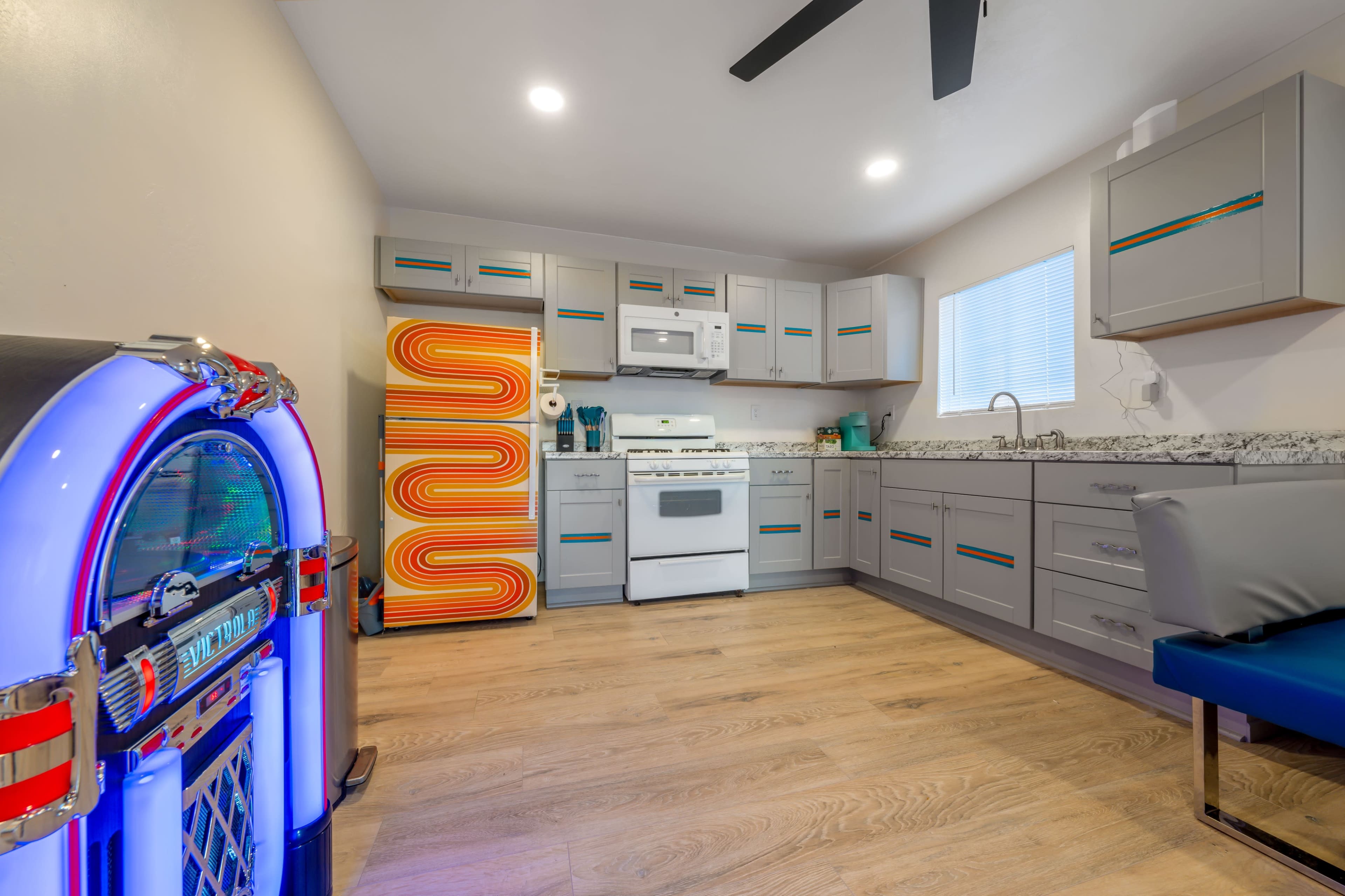 A modern kitchen featuring gray cabinets, a white appliance set, and a colorful vintage jukebox in the corner.