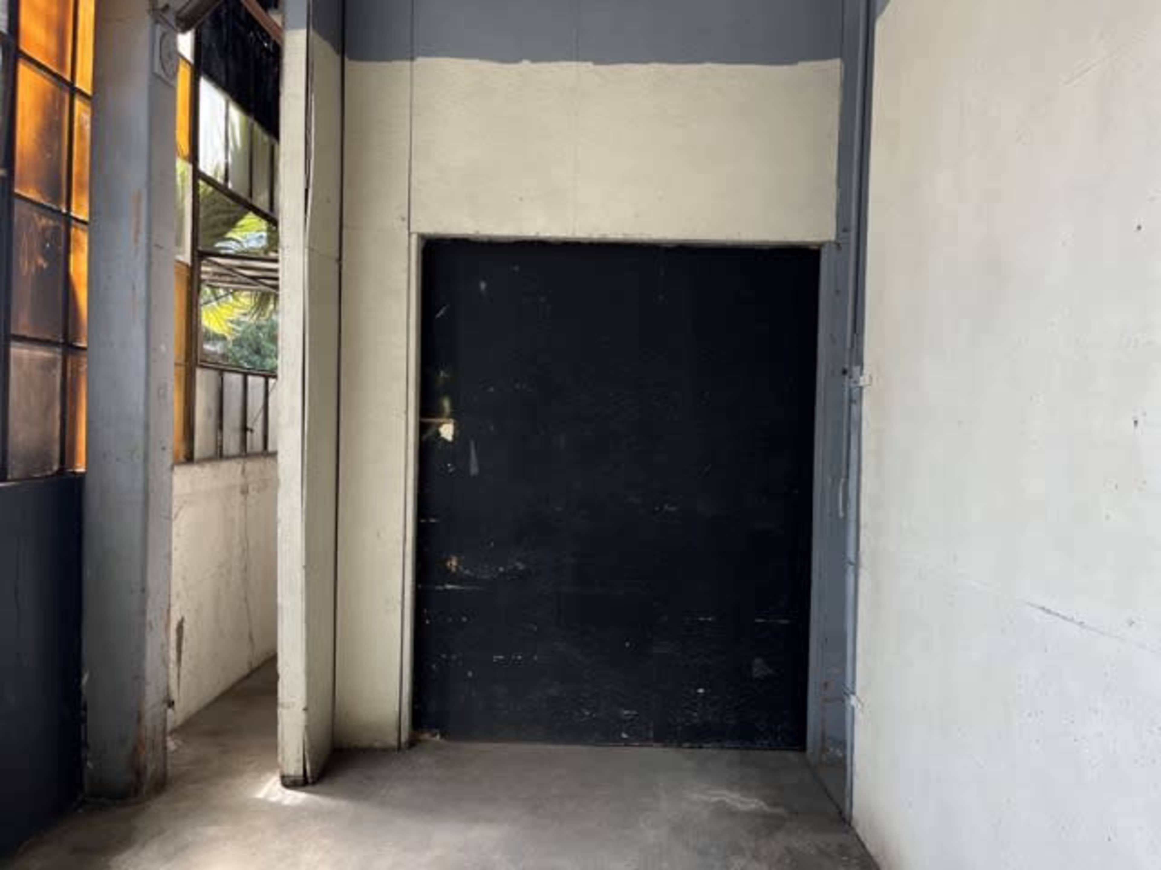 An empty room with a black door on one wall and large windows providing natural light on another wall.