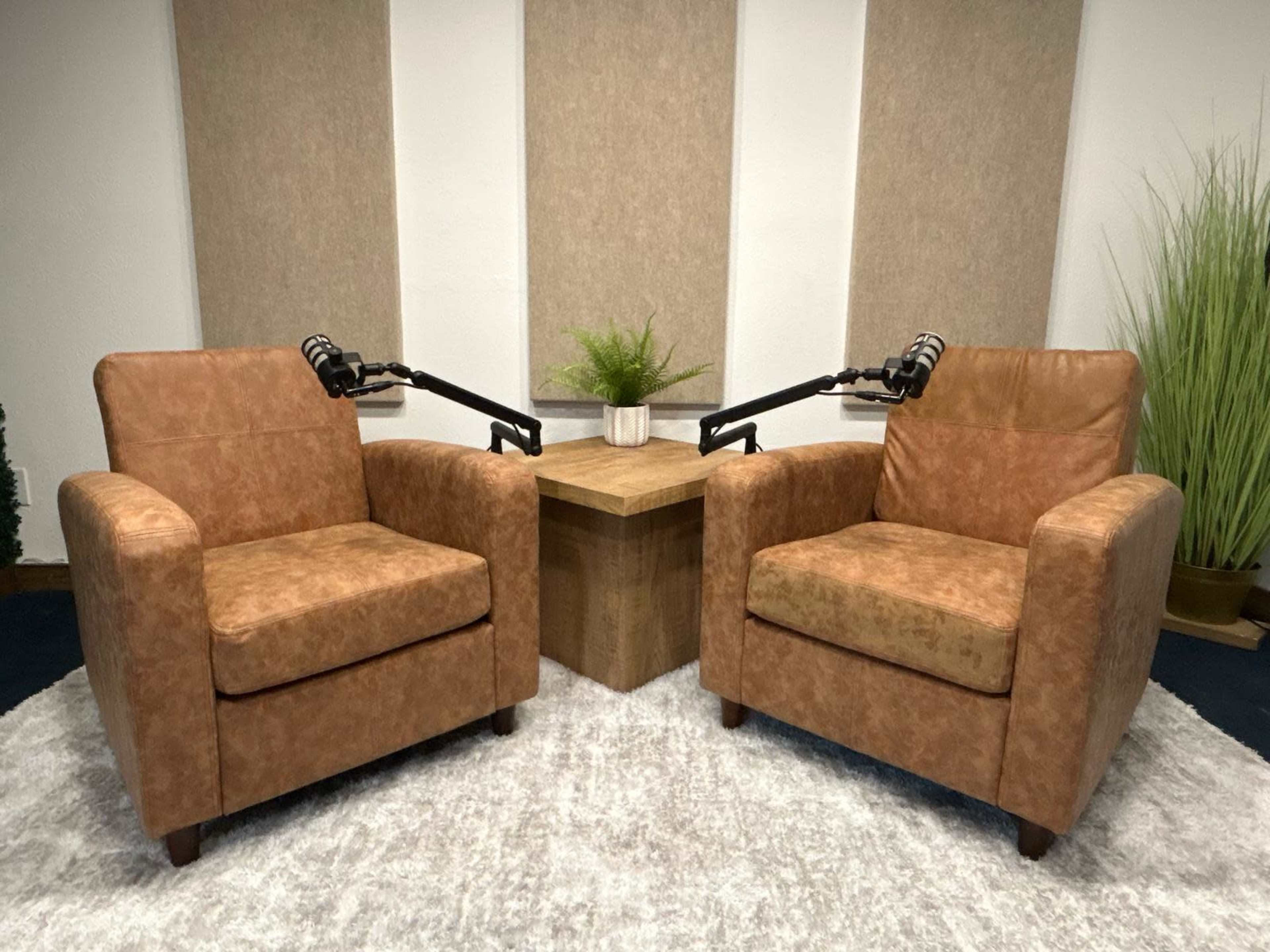 The image shows two brown armchairs positioned facing each other around a wooden coffee table in a room with wall panels and a small potted plant.