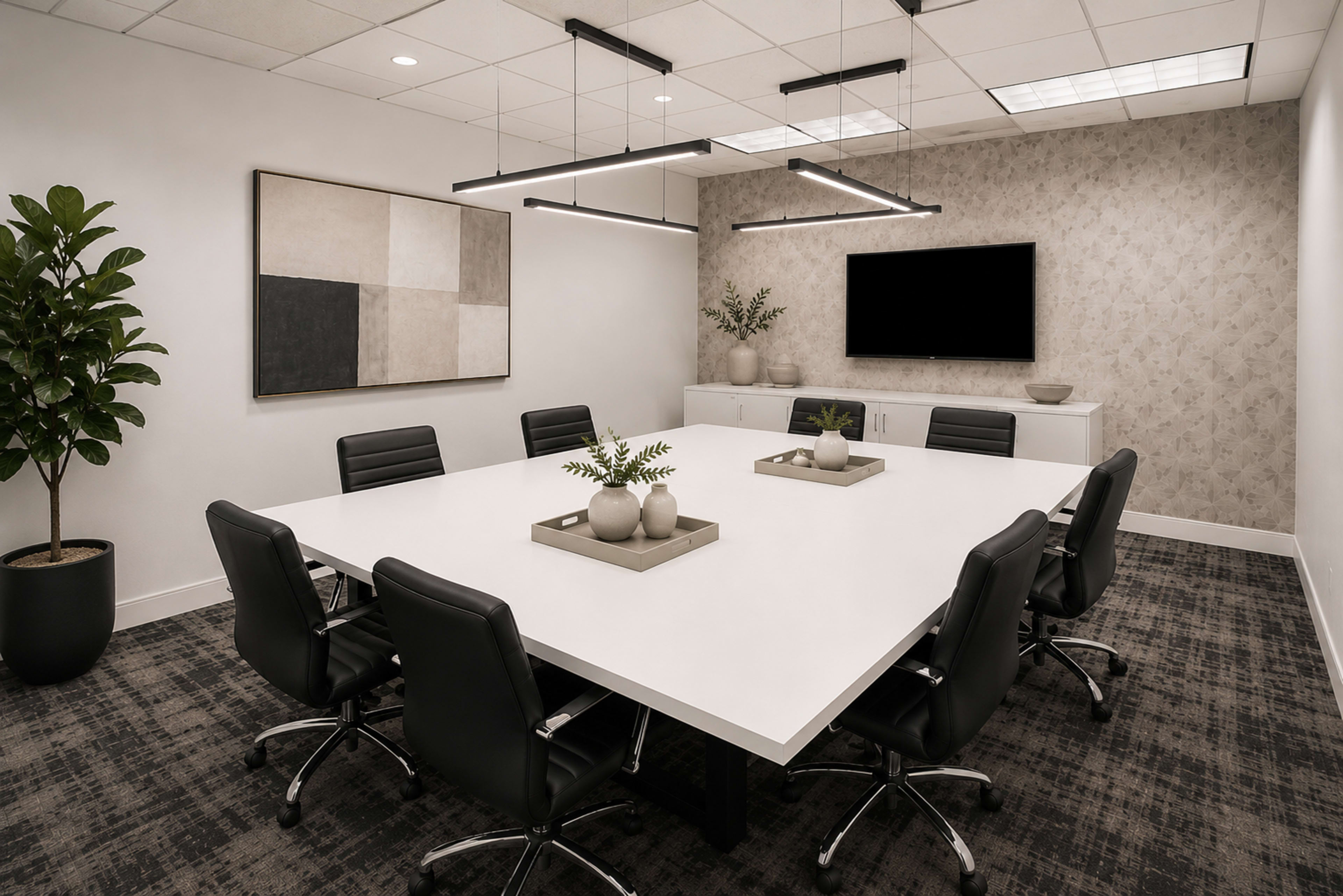 A modern conference room features a large white table surrounded by black swivel chairs, with minimalist decor including plants and framed artwork on the walls.