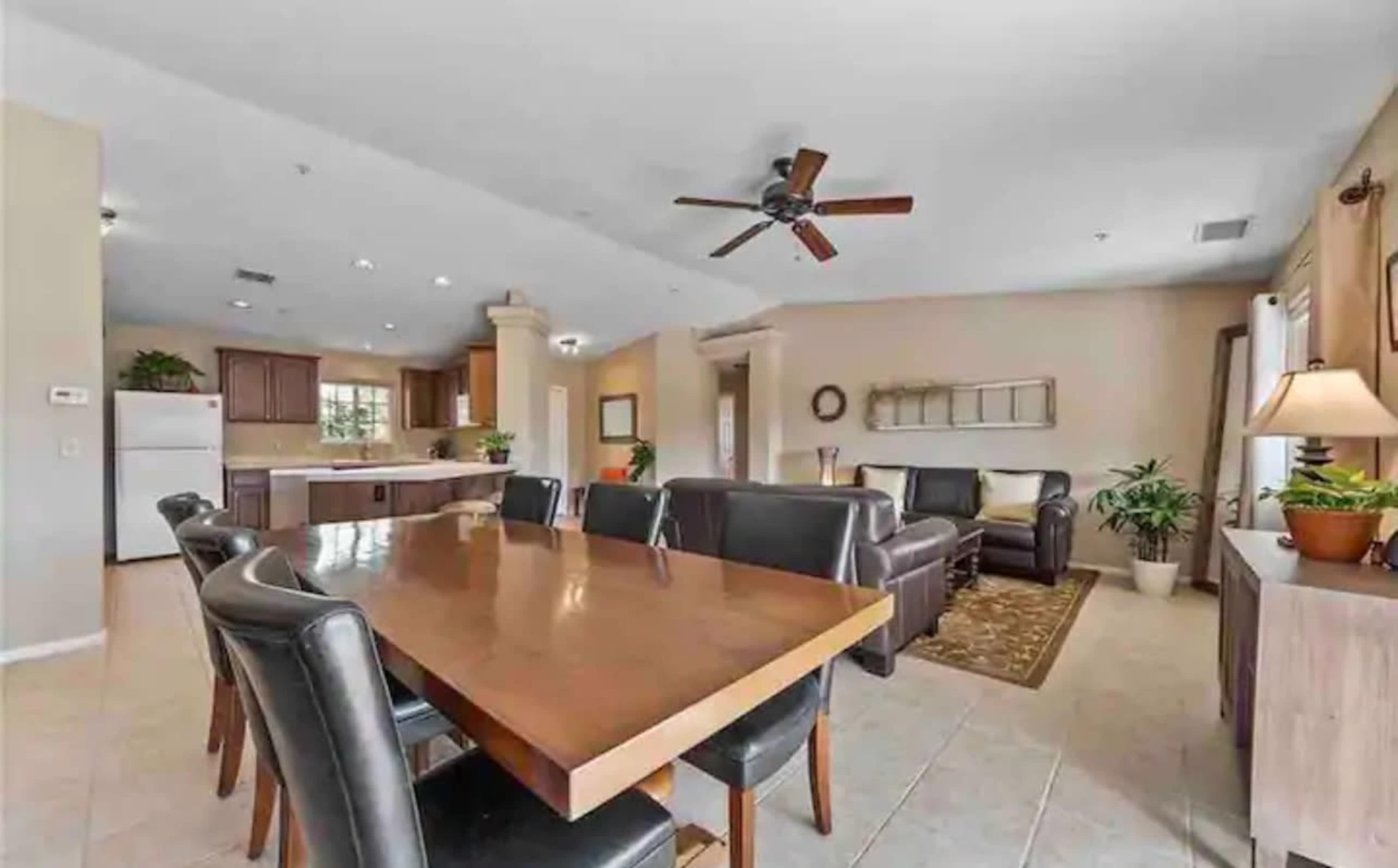 A modern open-concept living and dining area with a large wooden table and leather seating, accompanied by plants and neutral-colored walls.