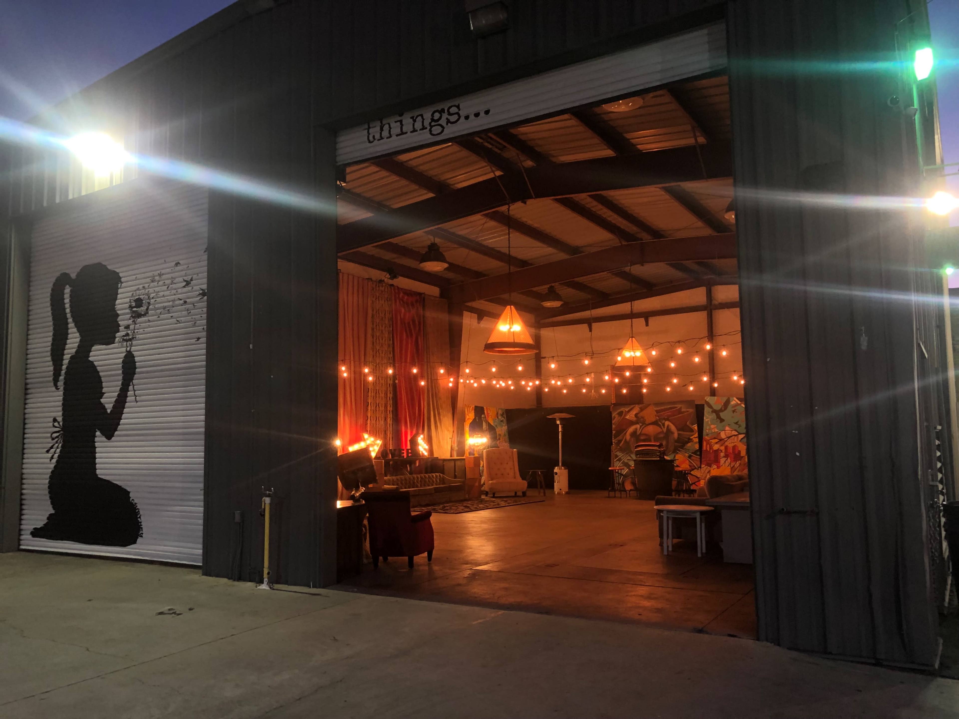 A large garage-style space features an open interior with decorative lighting and artwork, alongside a silhouette mural on the exterior wall.