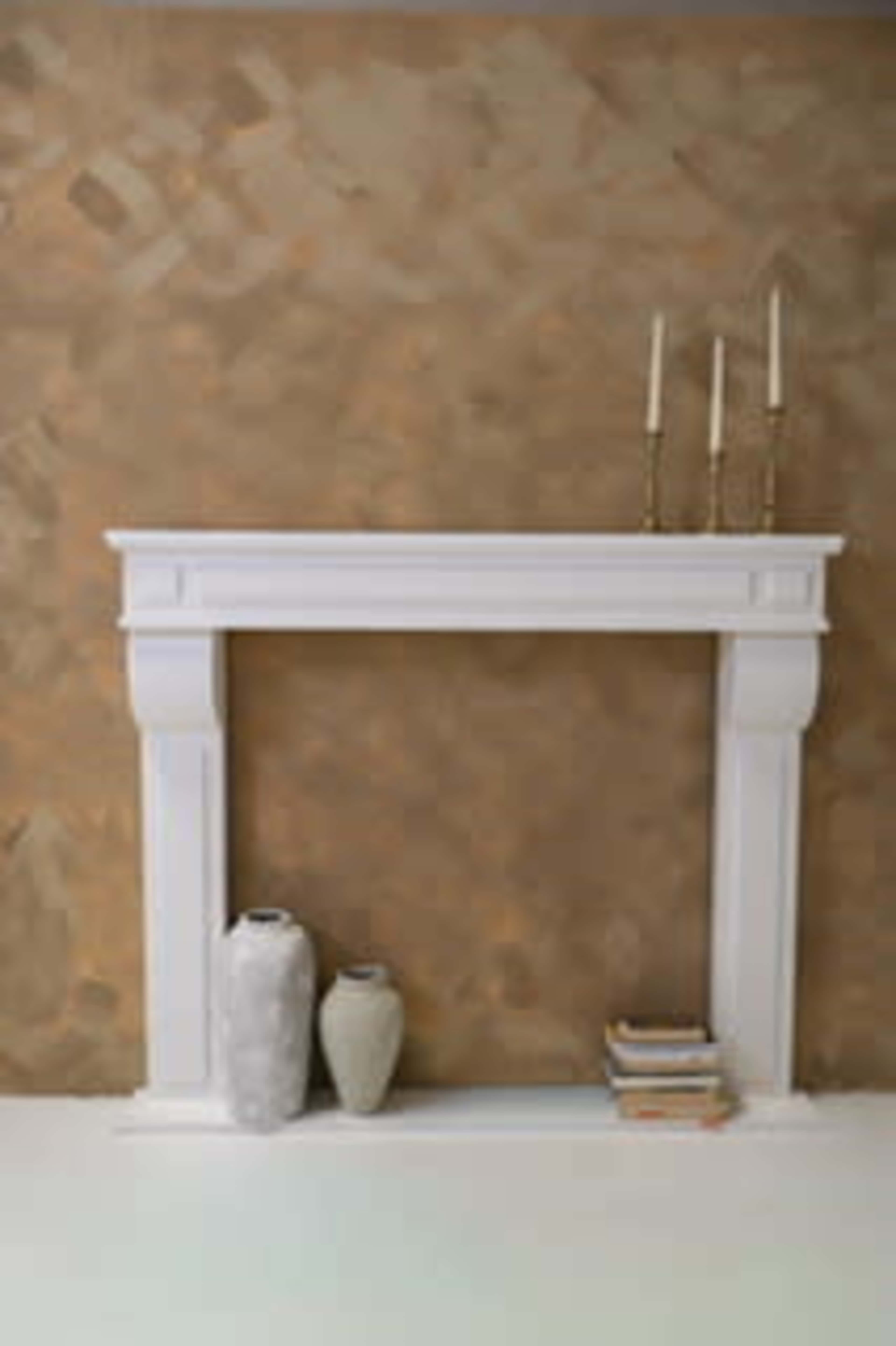 A white mantel with two decorative vases and stacked books is positioned against a textured brown wall.