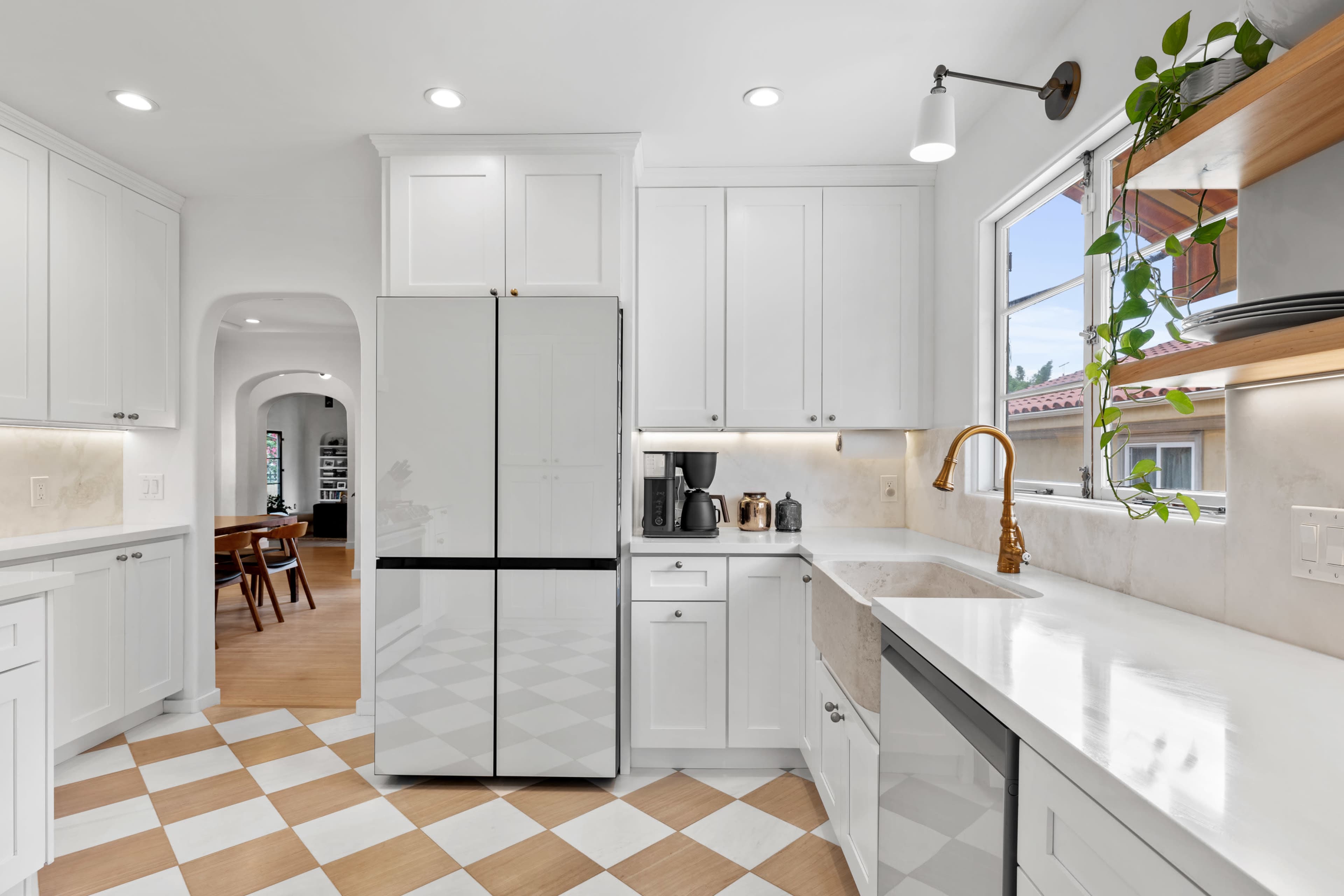 A modern kitchen features a black and white refrigerator, stainless steel appliances, and a checkered floor with light wood and white tiles.