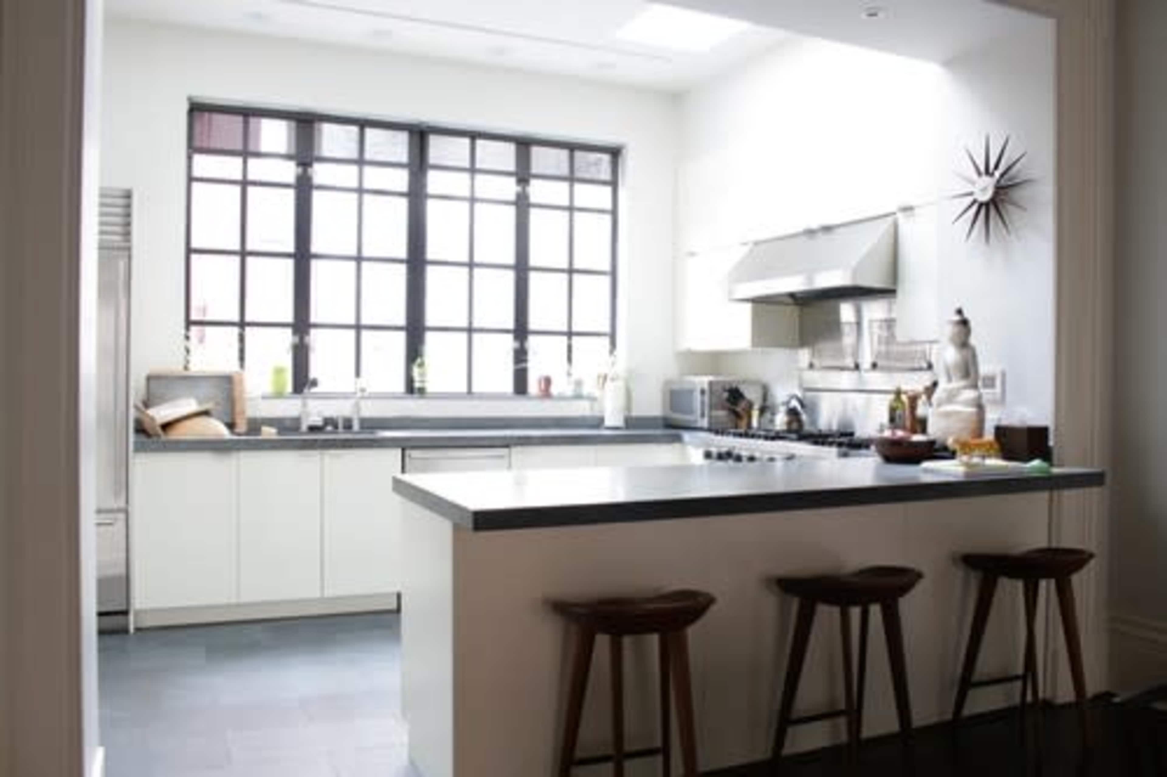 A modern kitchen with a central island, stainless steel appliances, and large windows allowing natural light.
