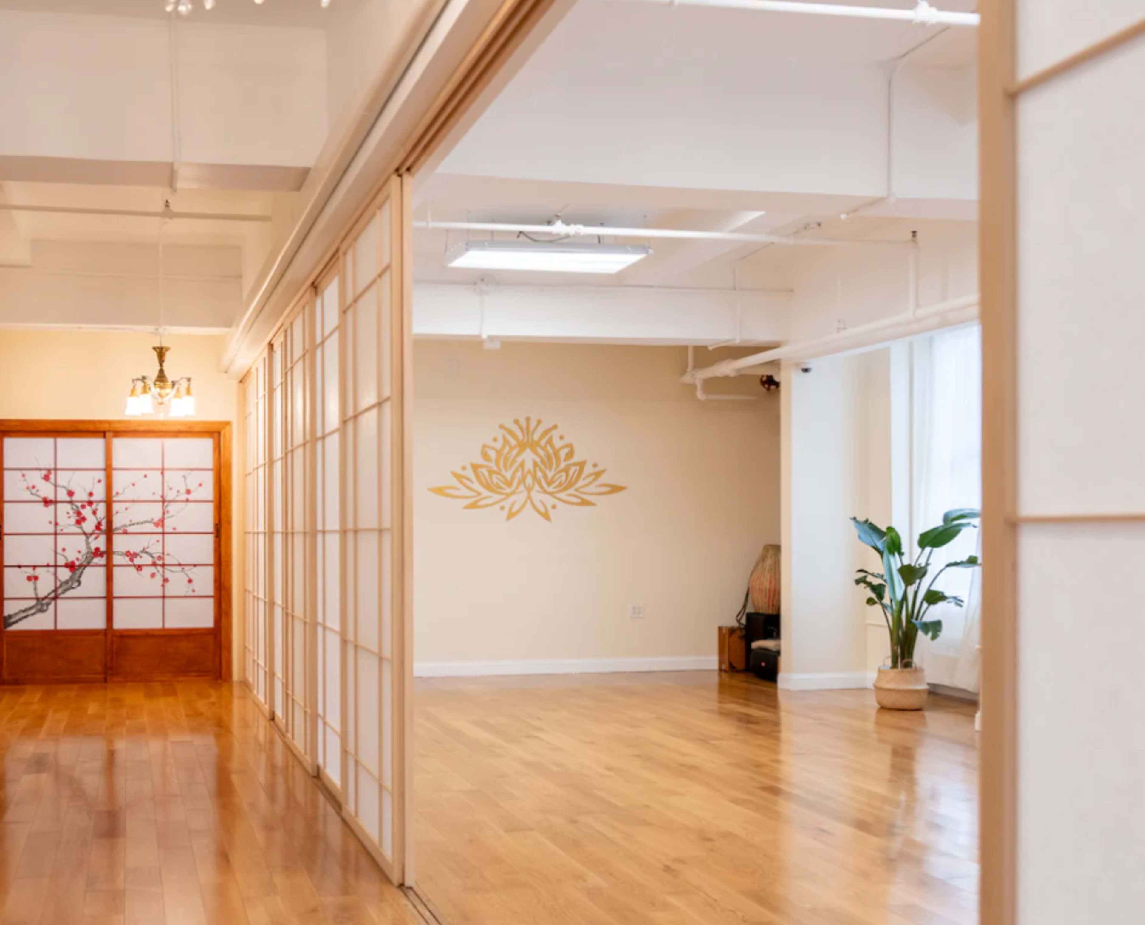 The image shows a spacious, well-lit studio with wooden floors, sliding shoji doors, and a decorative wall featuring a lotus design.