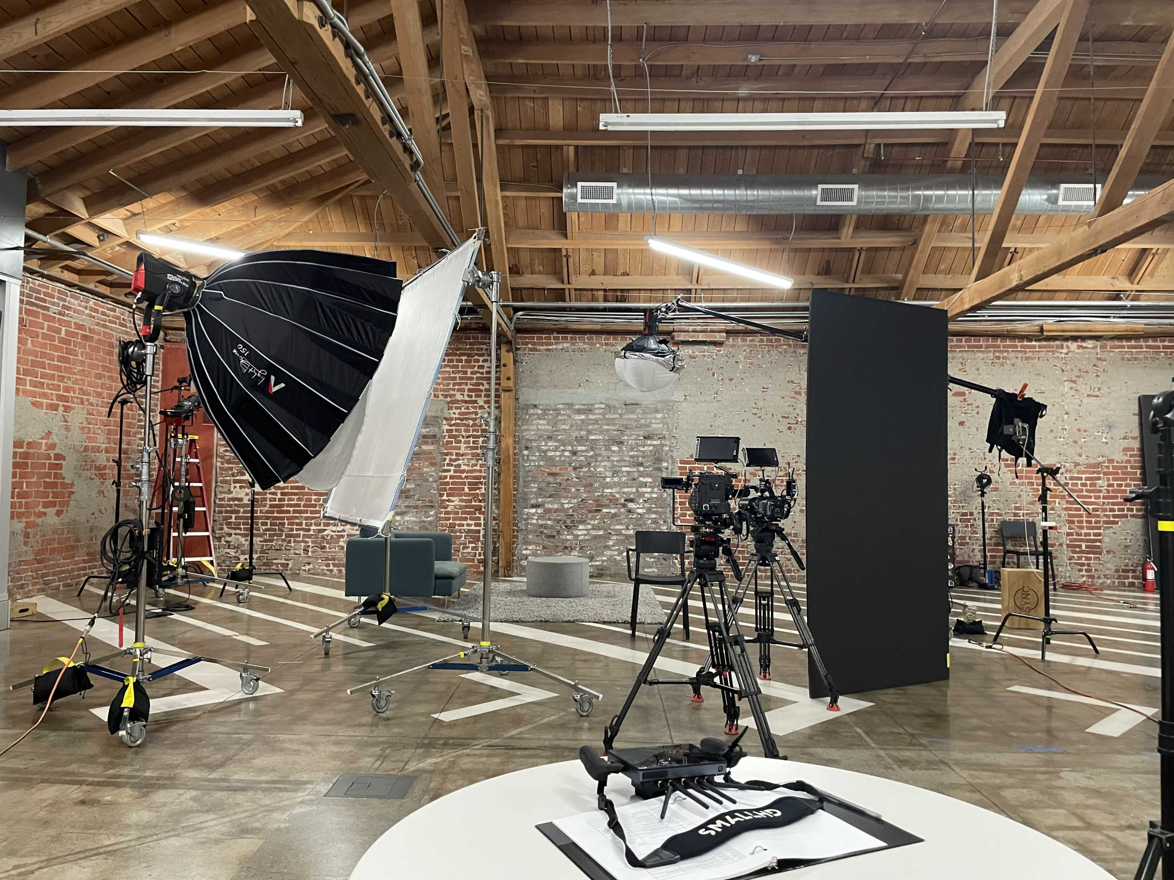 A photography studio featuring multiple cameras, lighting equipment, and a backdrop set against exposed brick walls.
