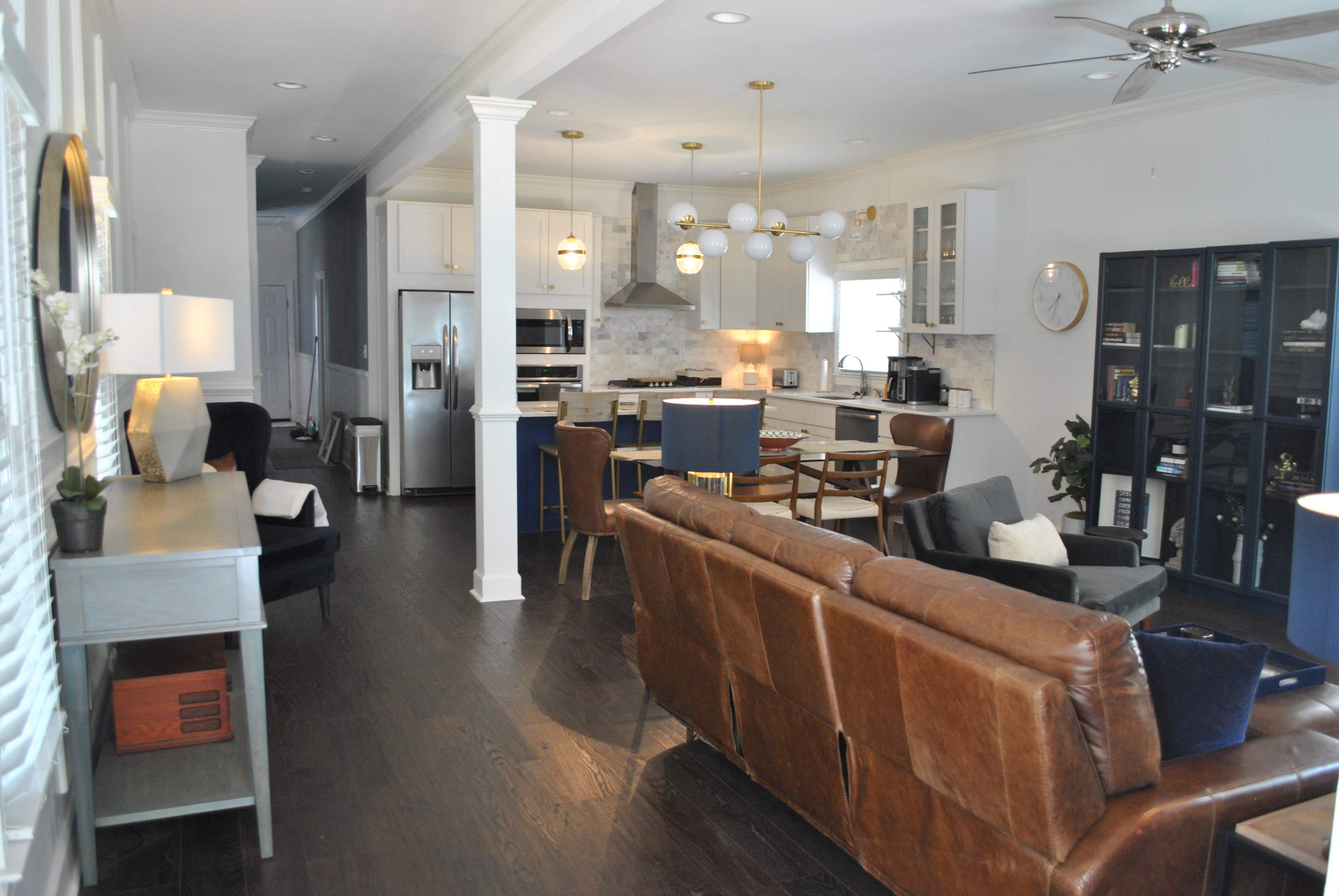 A modern open-concept living room and kitchen area featuring leather sofas, a dining table, and contemporary lighting fixtures.