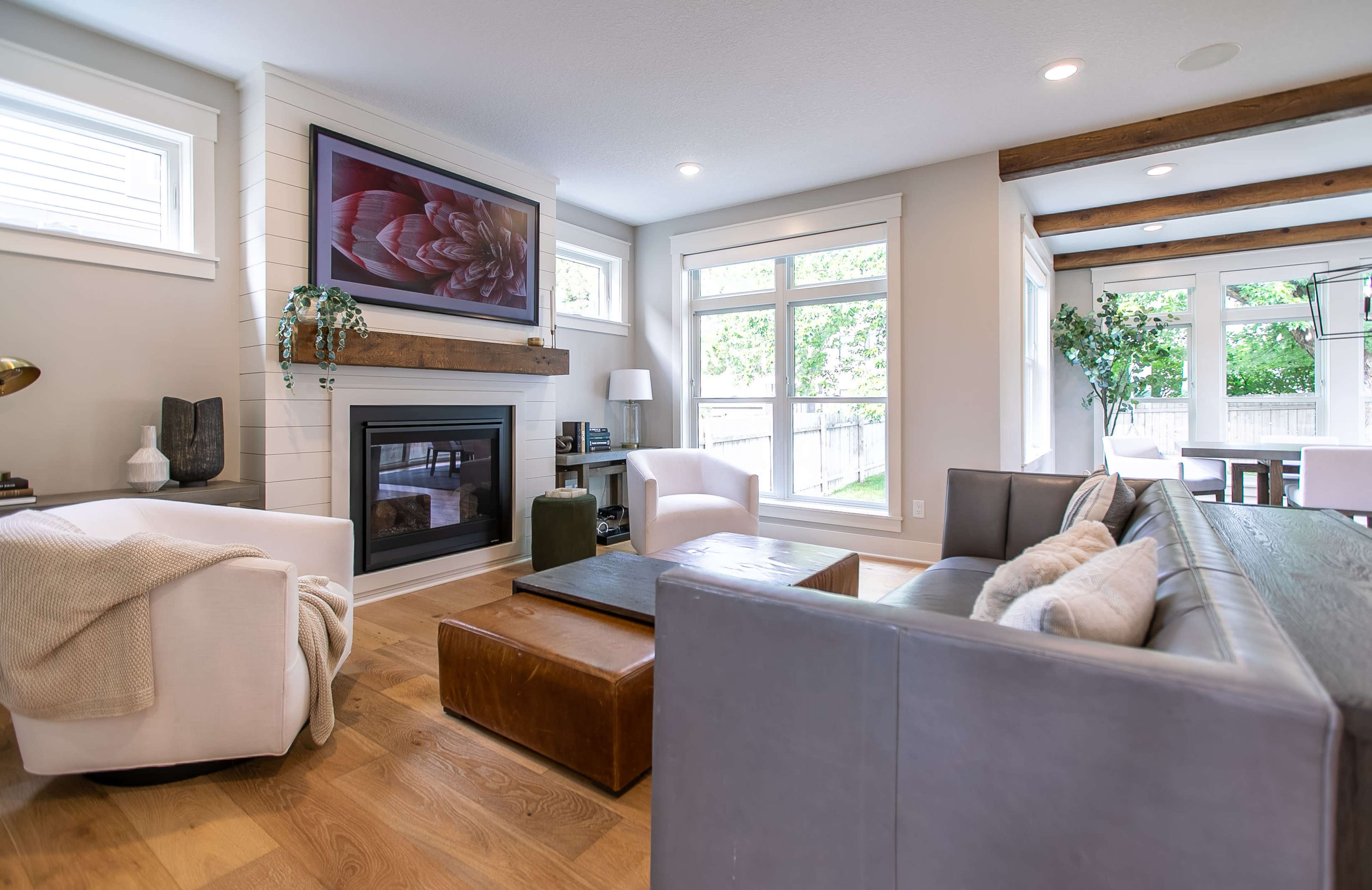 A modern living room with a fireplace, large windows, and a mix of light-colored furniture and wooden accents.