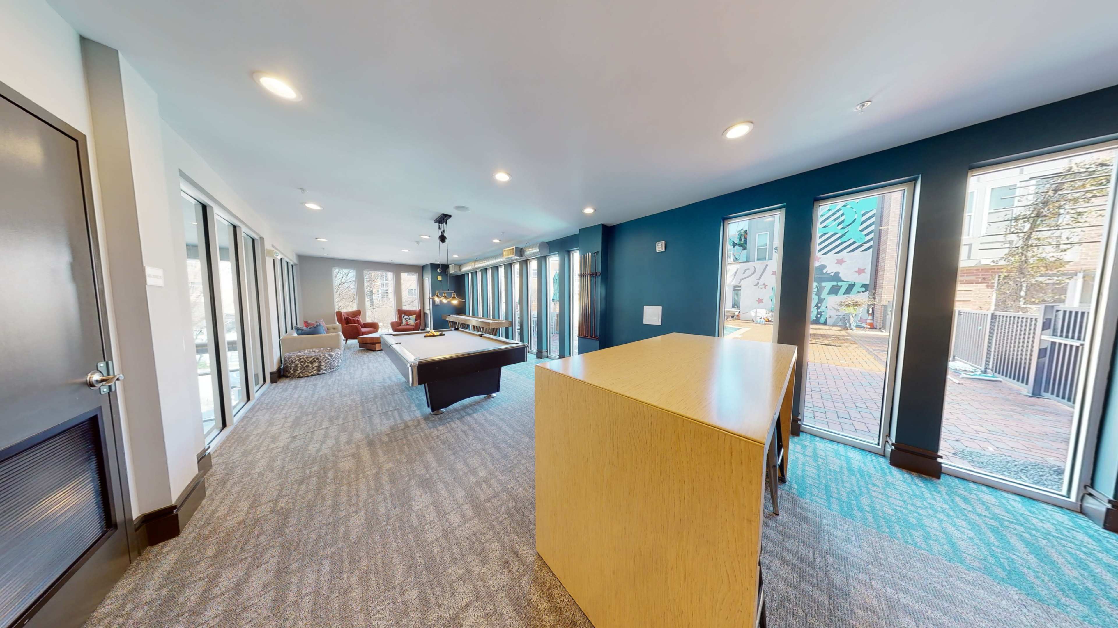 A modern common area with large windows, a pool table, and access to a courtyard.