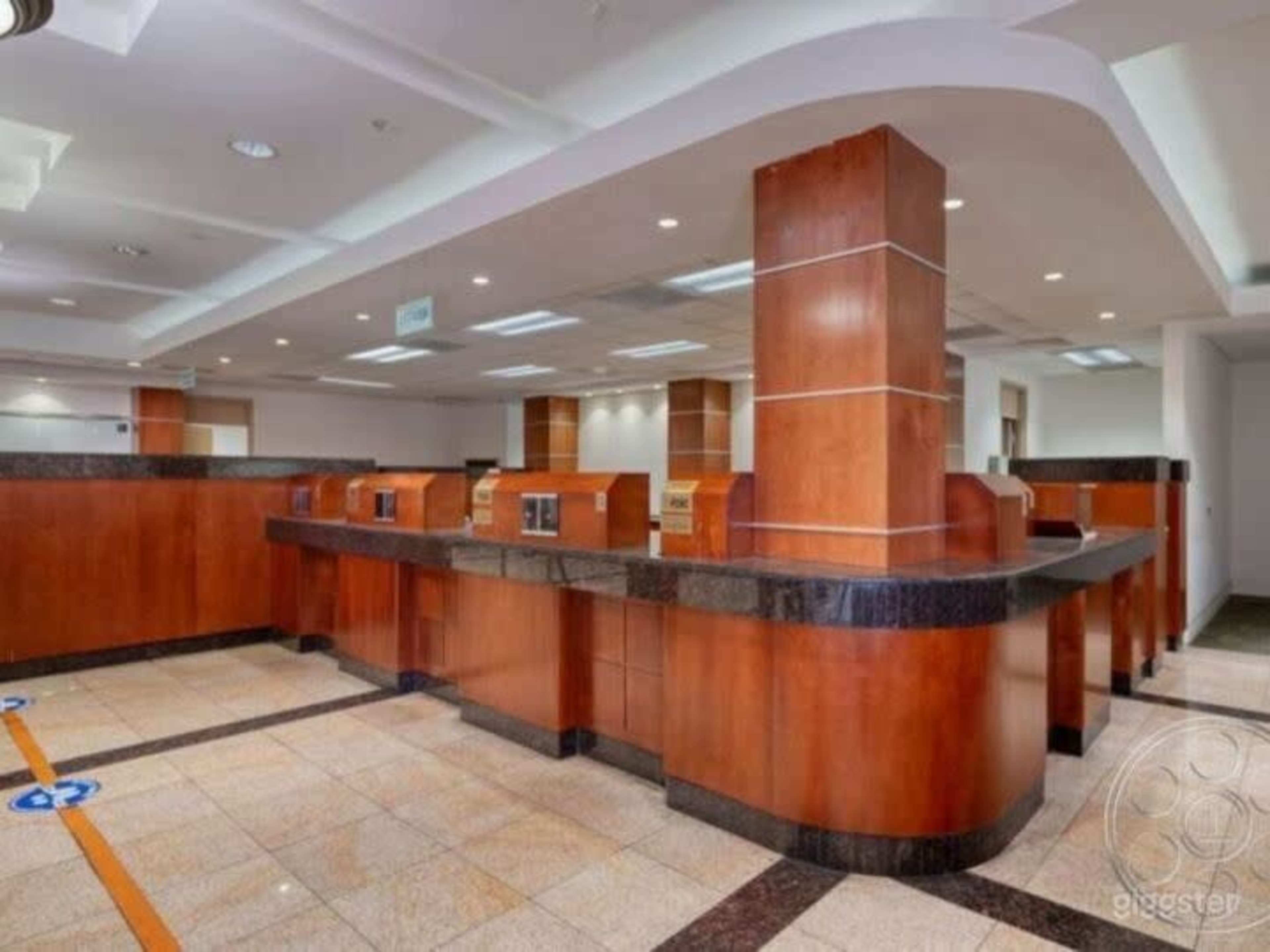 The image shows a spacious interior of a bank with wooden and granite counters, arranged in a semi-circular layout, and tile flooring.