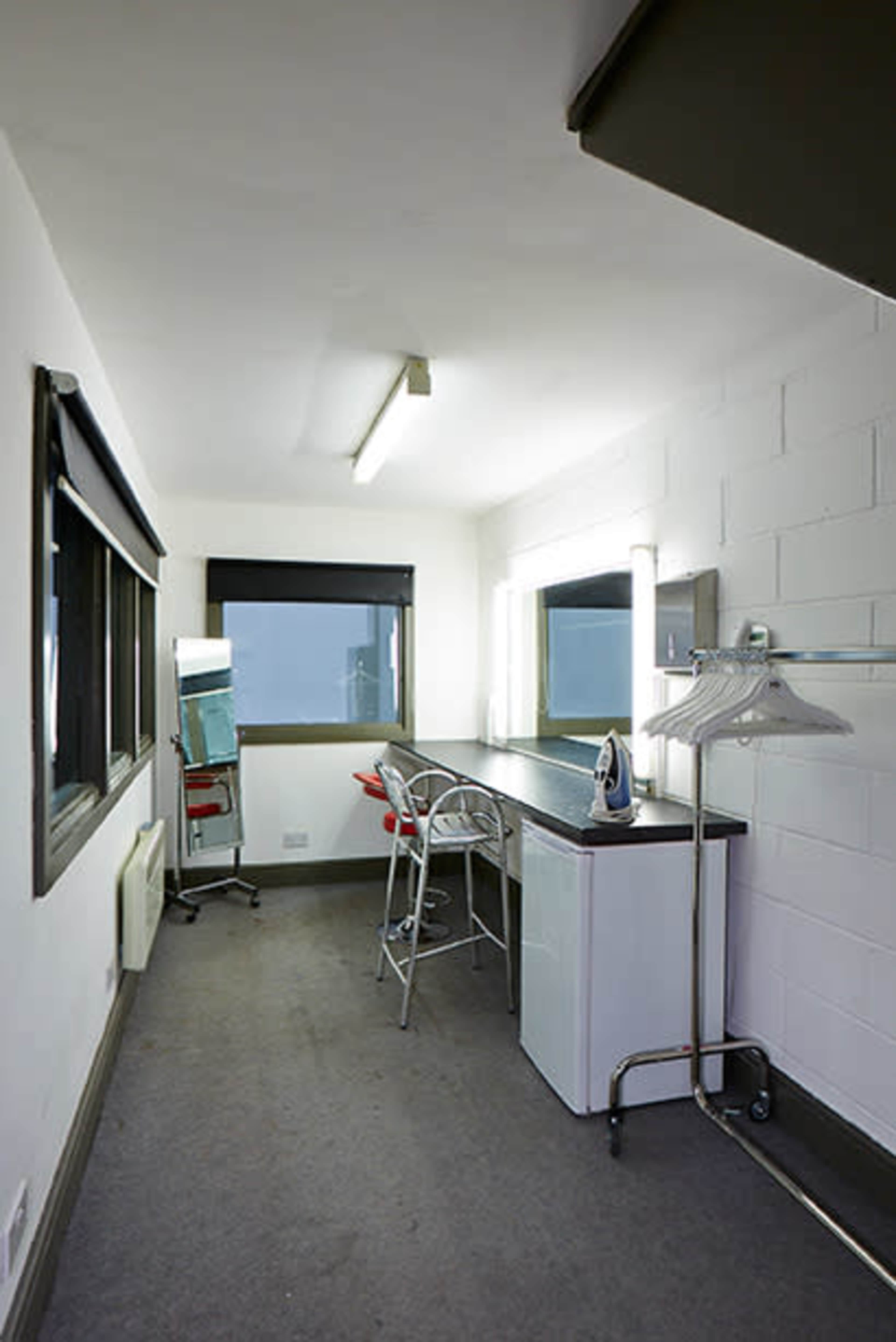 A small, minimalist dressing room with a countertop, two mirrors, a clothing rack, and a few chairs.