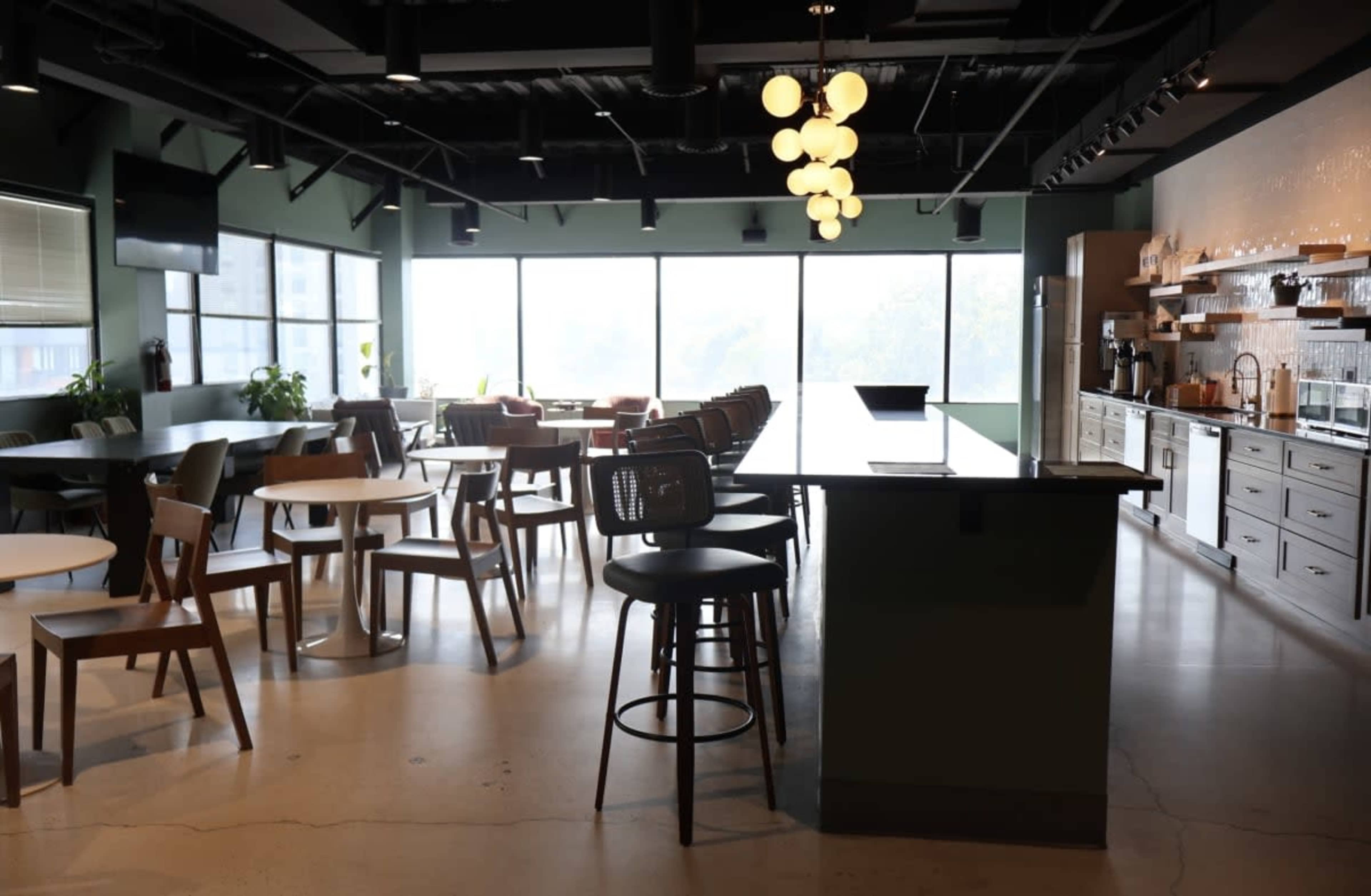 The image shows a modern cafe interior with various seating options and large windows allowing natural light to enter.