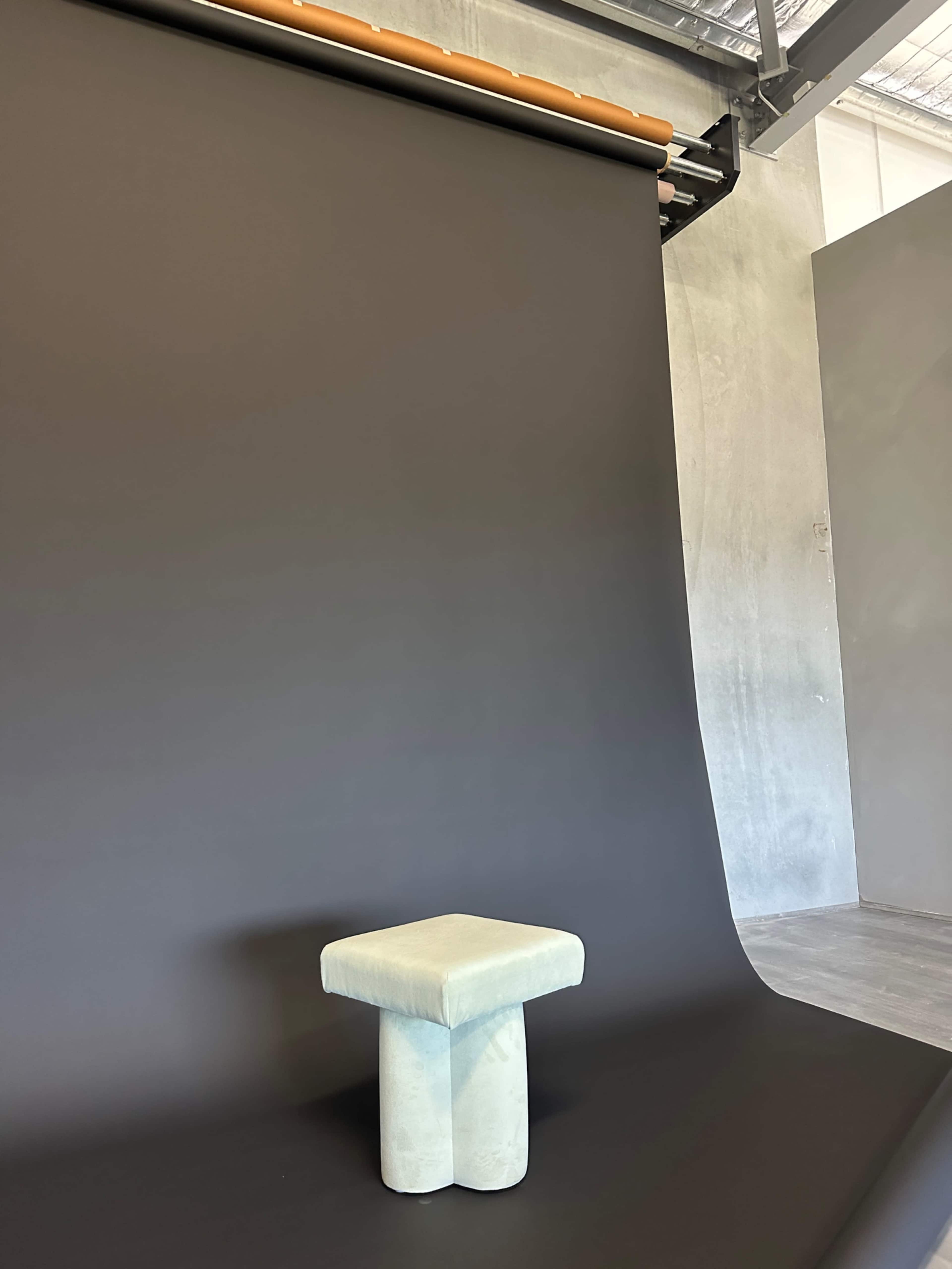 A light blue stool stands on a dark backdrop in a spacious studio.