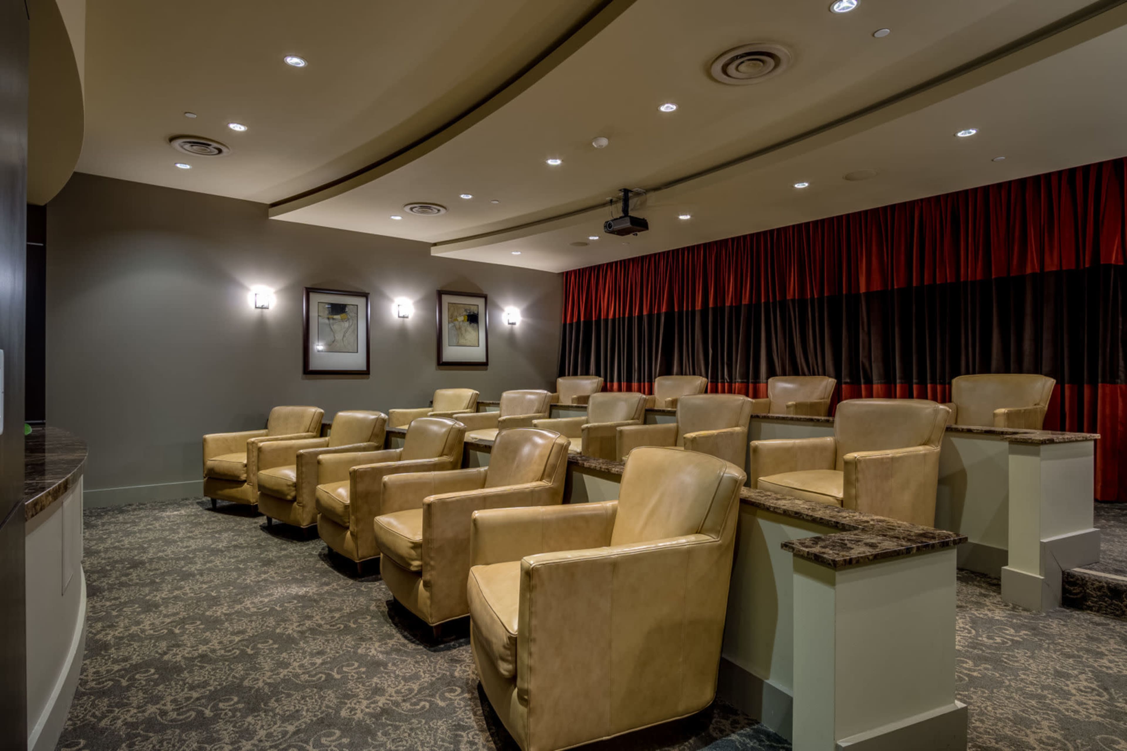 A small, comfortably arranged theater features plush beige chairs, a dark carpet, and red and black drapes.