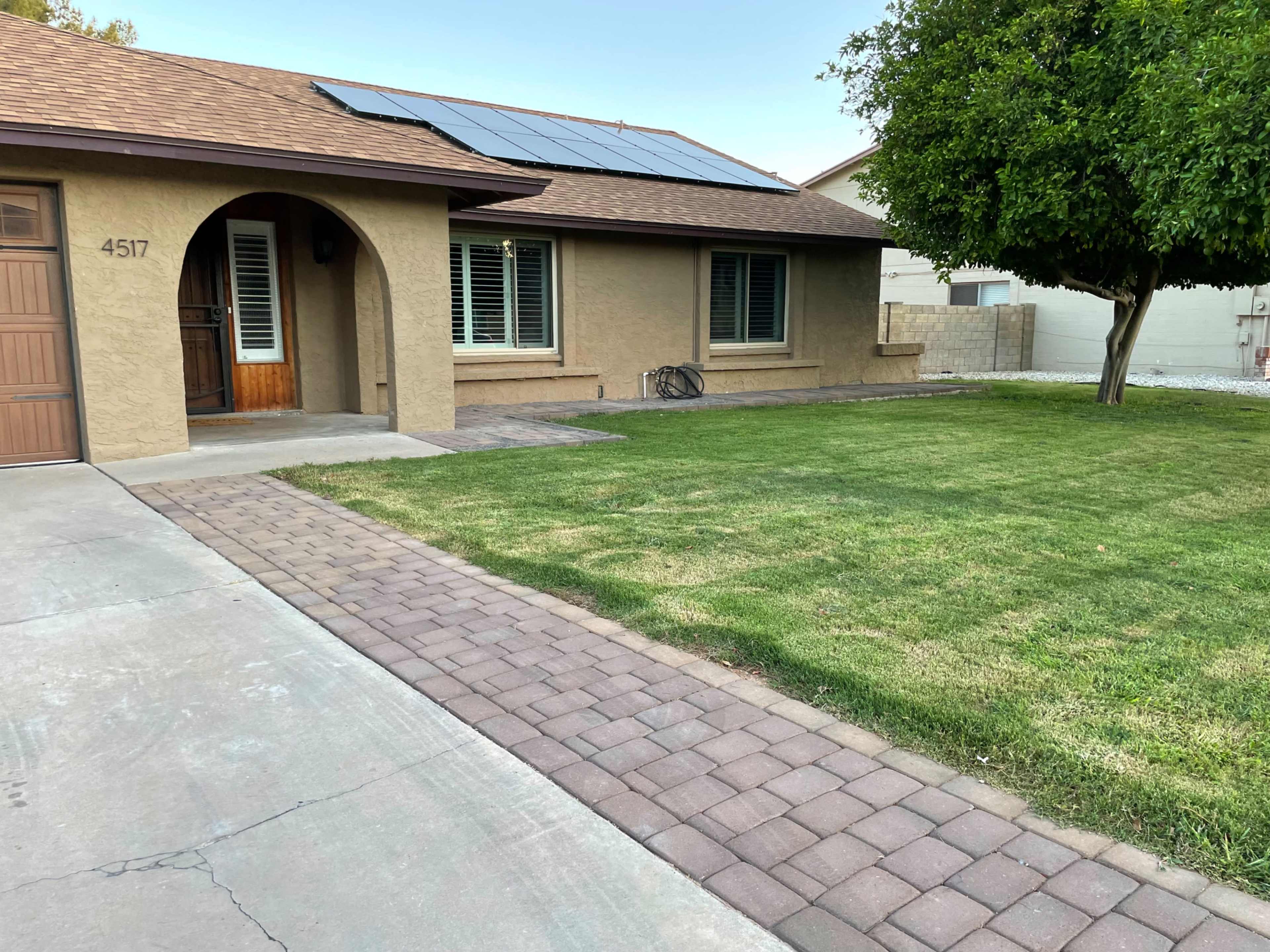 A single-story house with a brown stucco exterior, a paved driveway, and a neatly maintained lawn featuring solar panels on the roof.