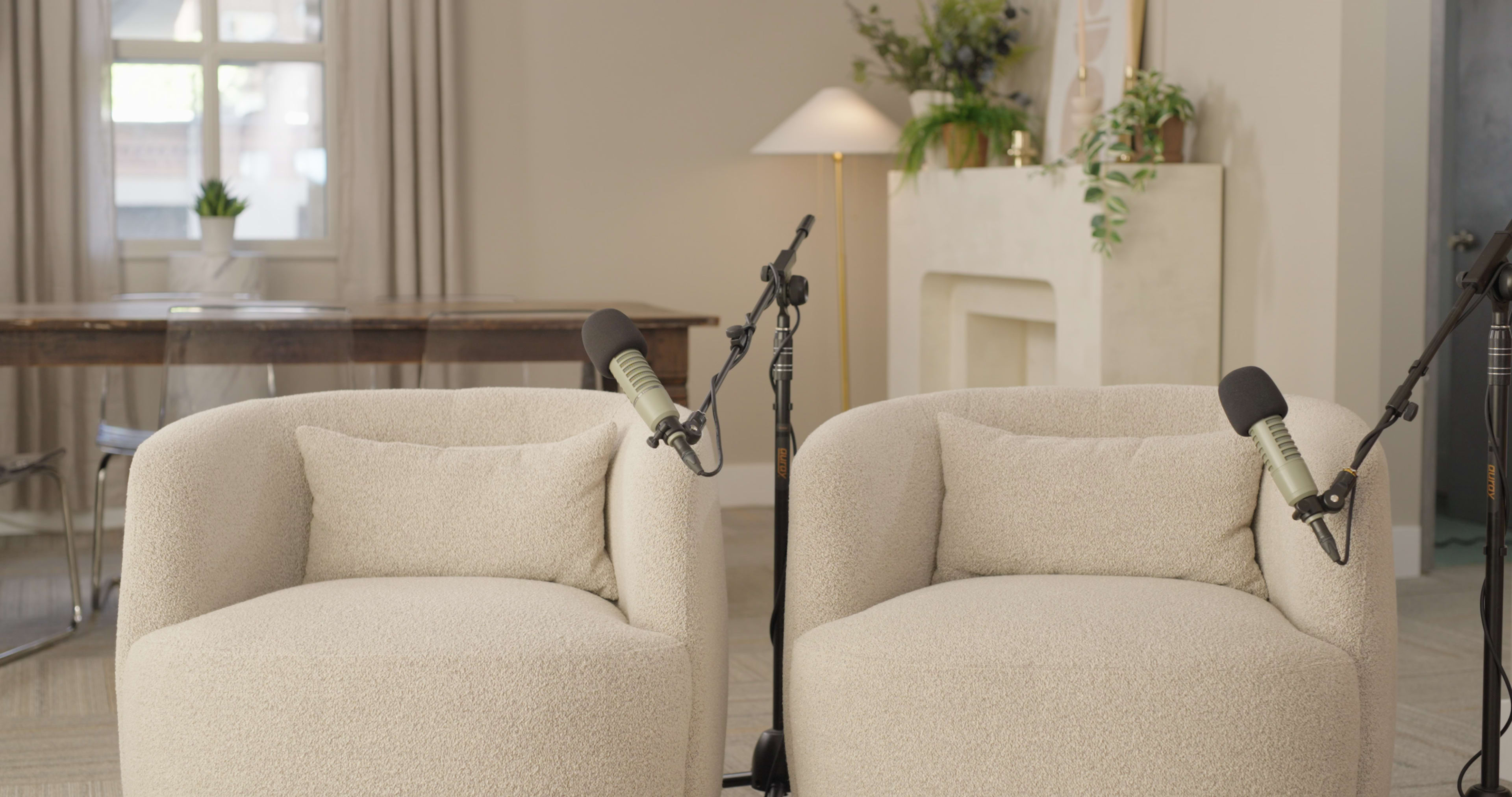 The scene features two light-colored, textured armchairs positioned in a room with a softly lit ambiance, accompanied by a microphone on a stand nearby.