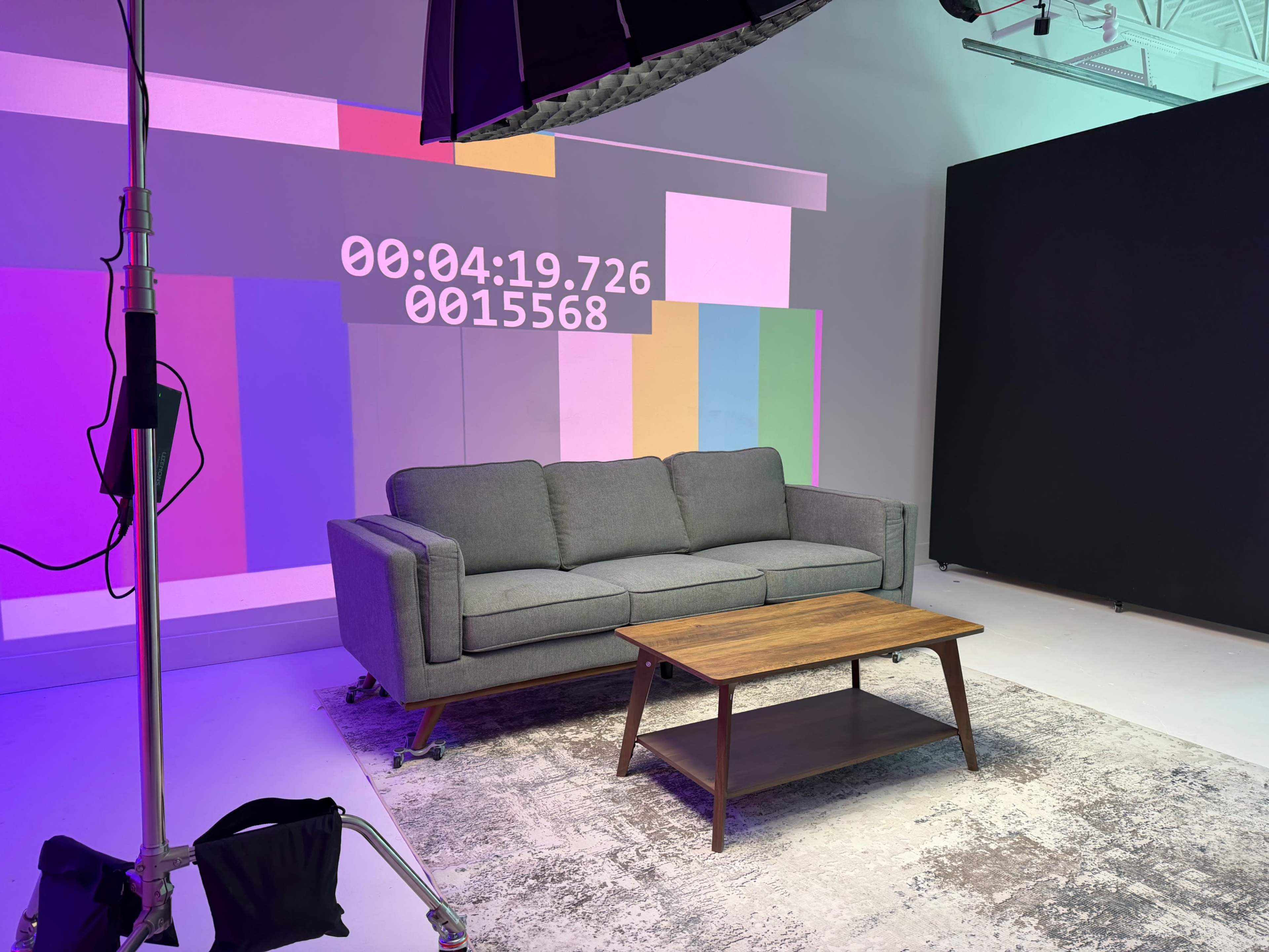 The image shows a gray sofa and a wooden coffee table set against a colorful backdrop with timing information displayed.