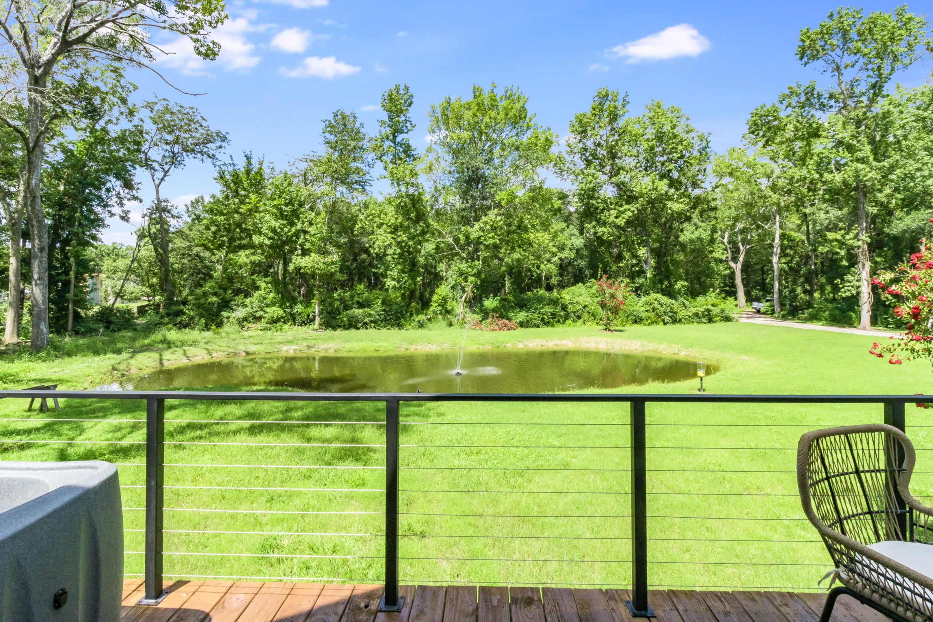 A view from a balcony overlooks a pond surrounded by trees and grass.